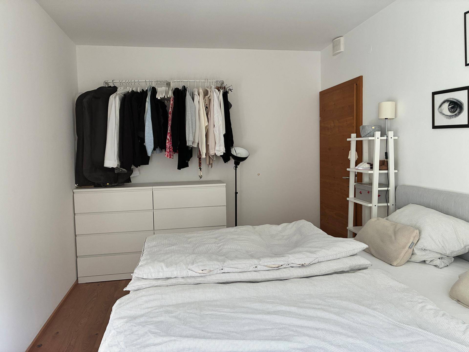 Schlafzimmer mit Holzboden, Kleiderstange und Kommode, hell und funktional eingerichtet.