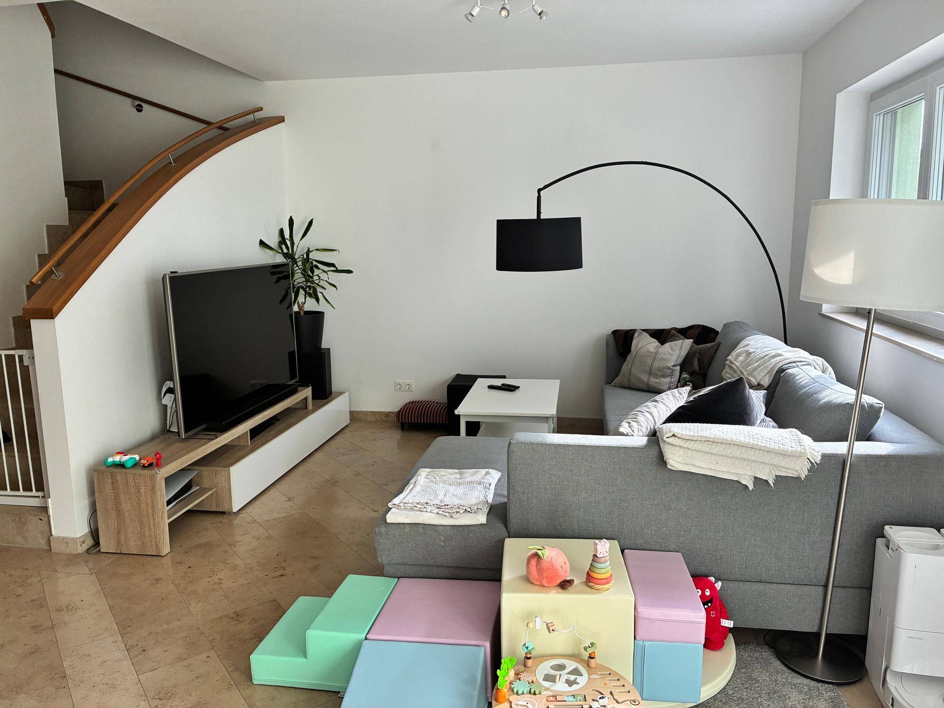 Gemütliches Wohnzimmer mit großem Sofa, Fernseher und Treppe zum Obergeschoss.