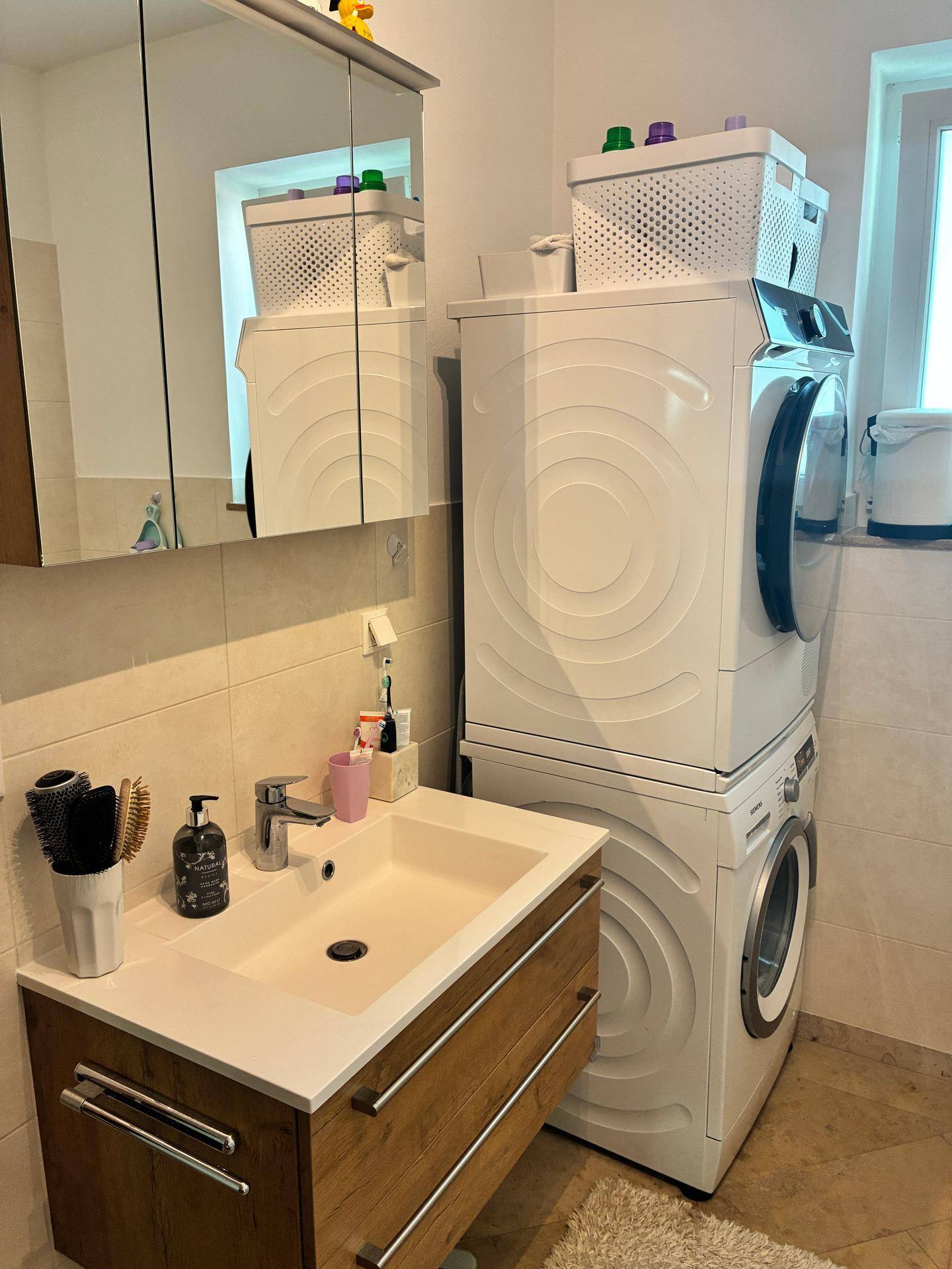 Badezimmer mit Waschbecken, Spiegelschrank und gestapelter Waschmaschine und Trockner.