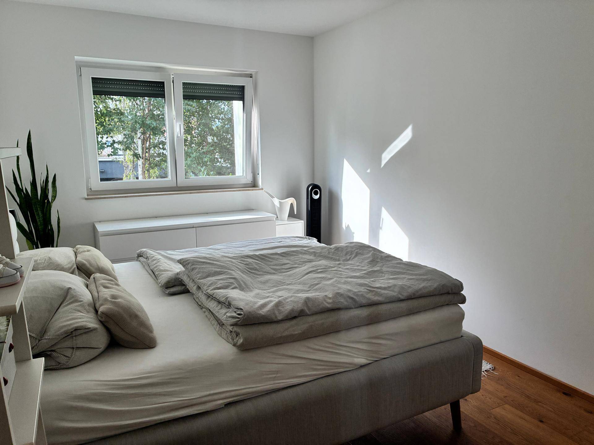 Helles Schlafzimmer mit Holzboden, großem Fenster und Blick ins Grüne.