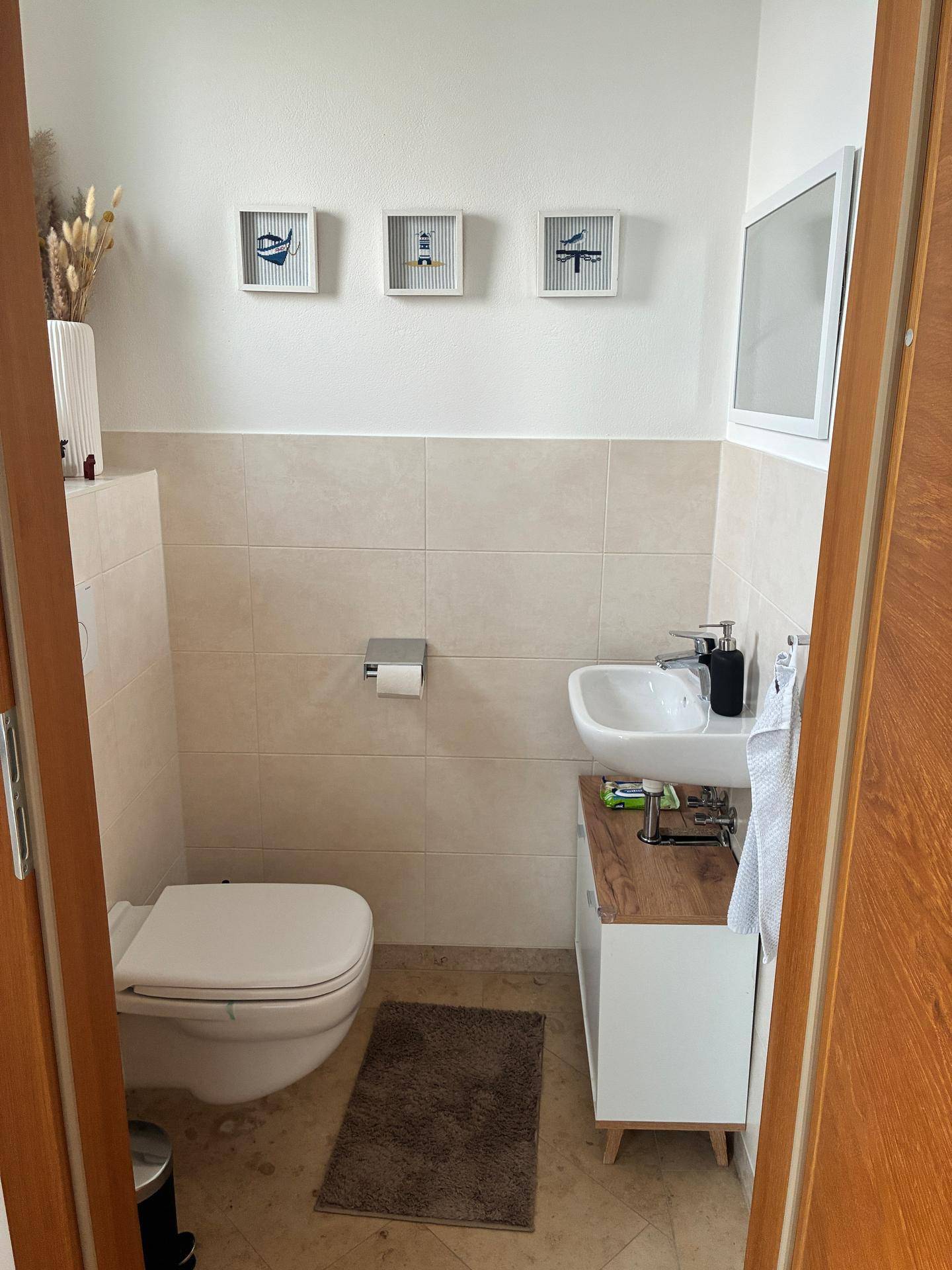 Modernes Gäste-WC mit beigen Fliesen, wandhängendem WC und kleinem Waschbecken.