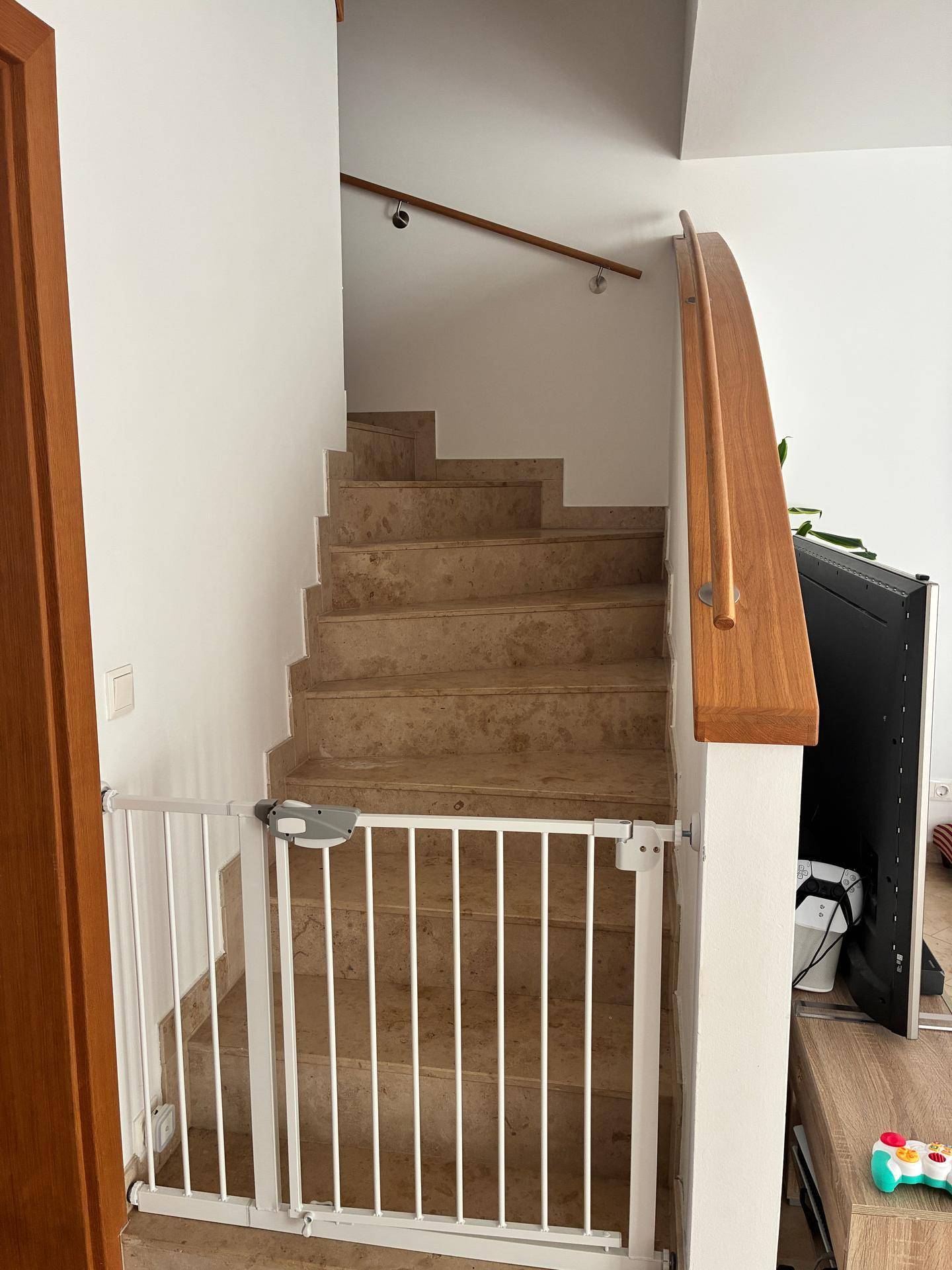 Treppenaufgang mit Fliesenstufen, Holzgeländer und Kinderschutzgitter.