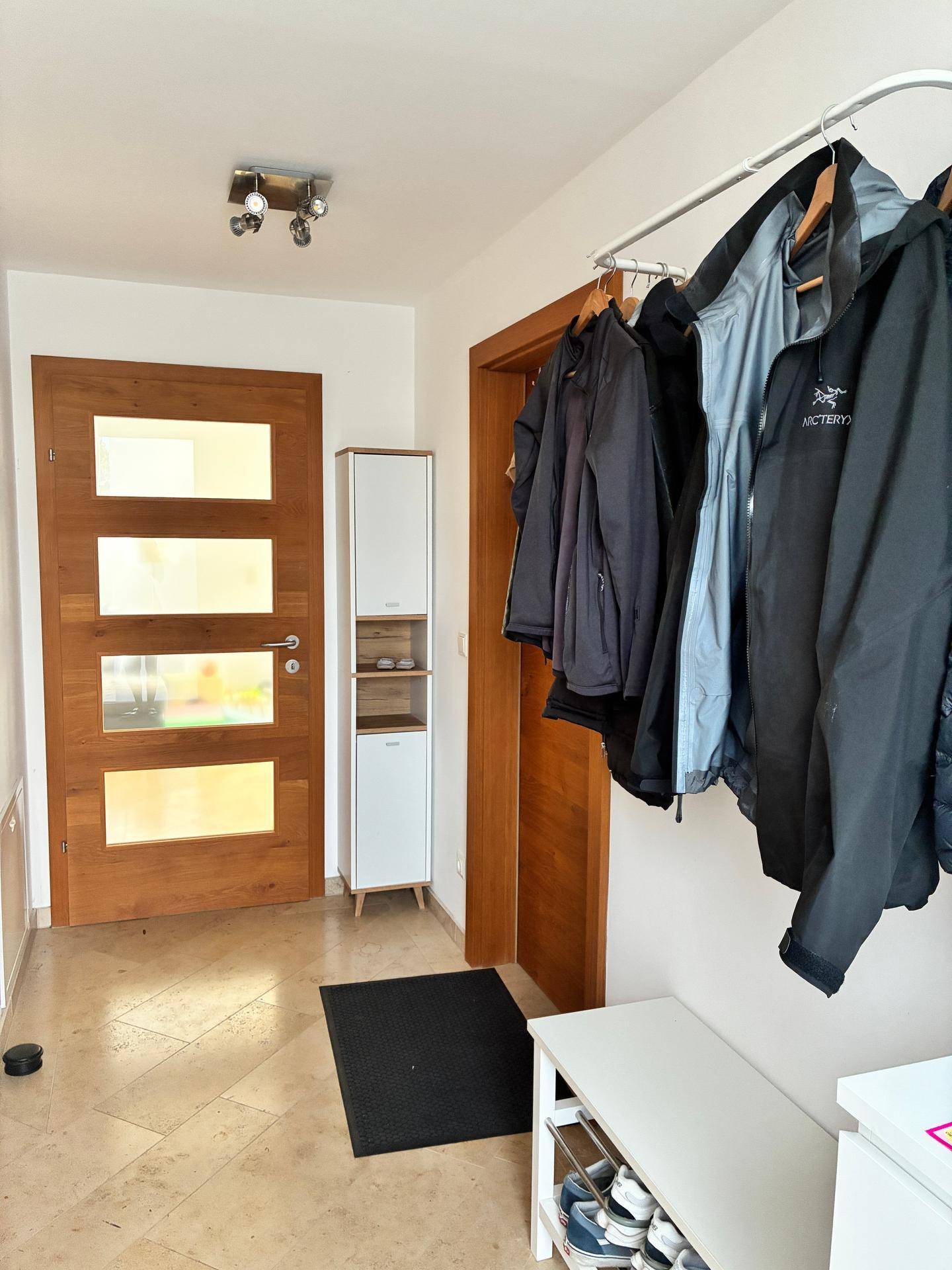 Heller Flur mit Fliesenboden, Garderobe und Holztüren mit Glaseinsätzen.