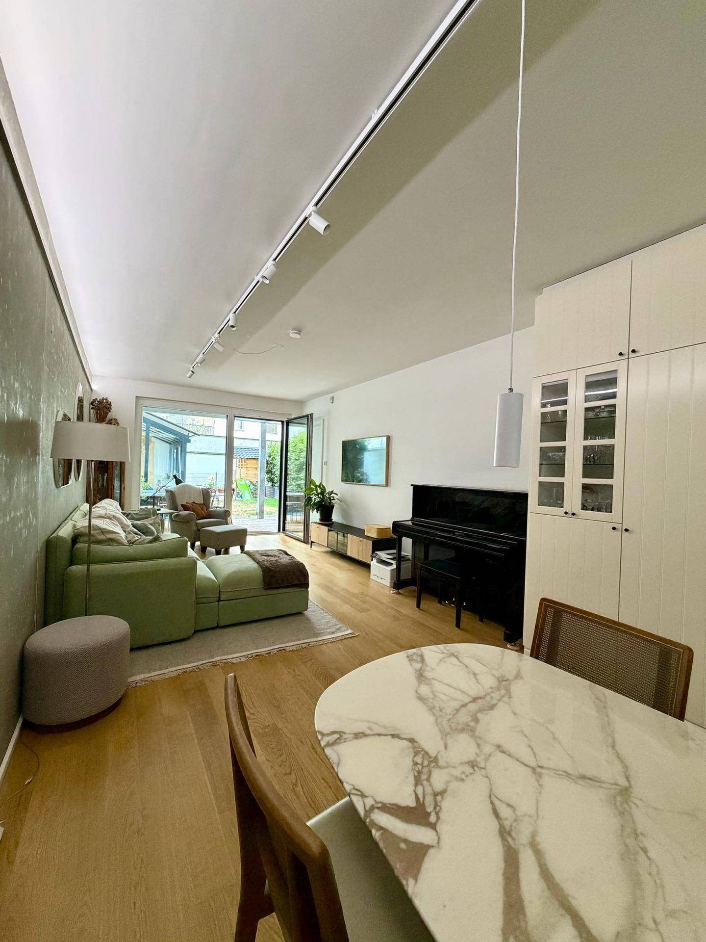 Gemütliches Wohnzimmer mit grünem Sofa, Klavier und direktem Zugang zum Garten.