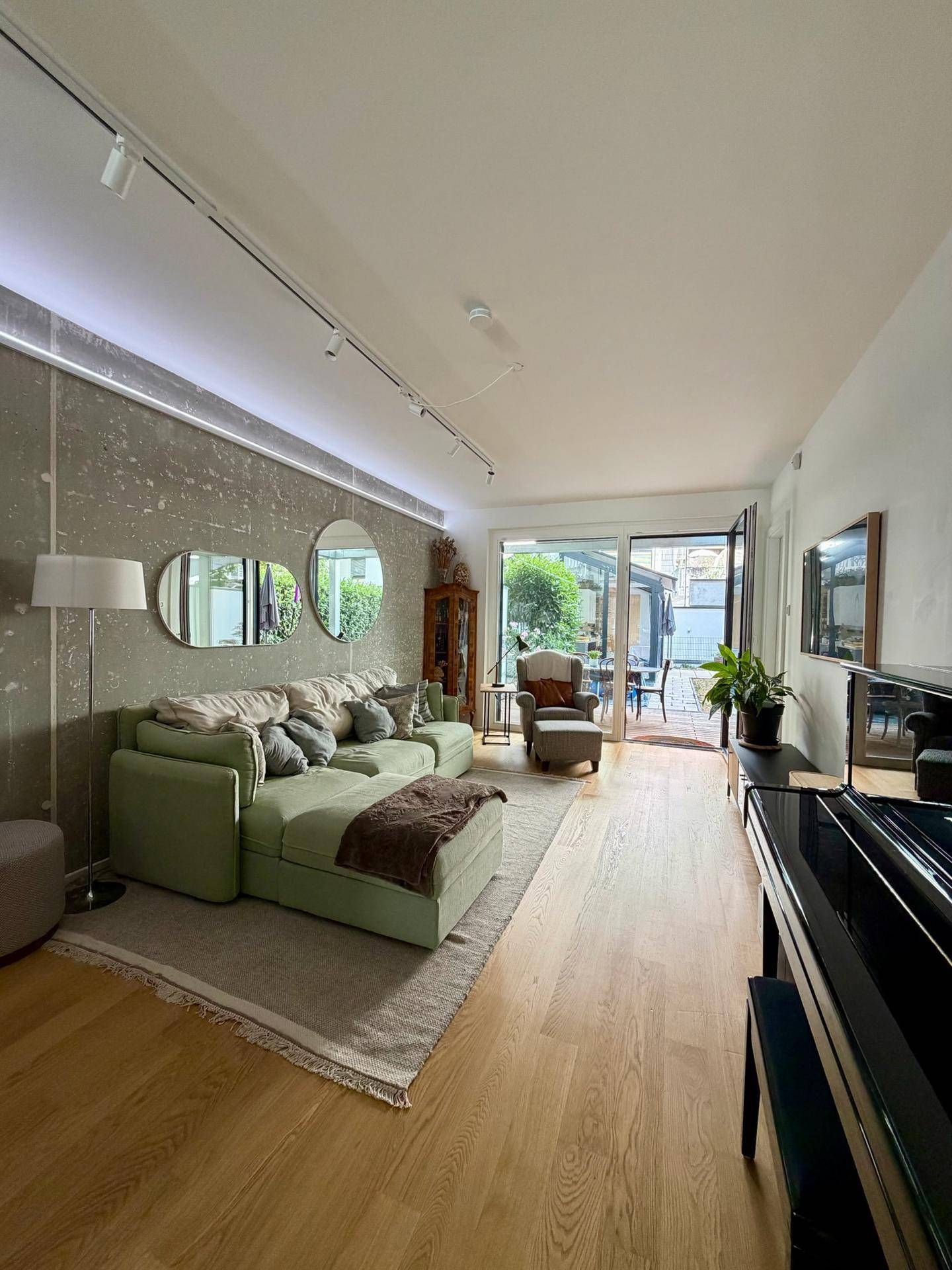 Geräumiges Wohnzimmer mit großem grünem Ecksofa und dekorativen Wandspiegeln.