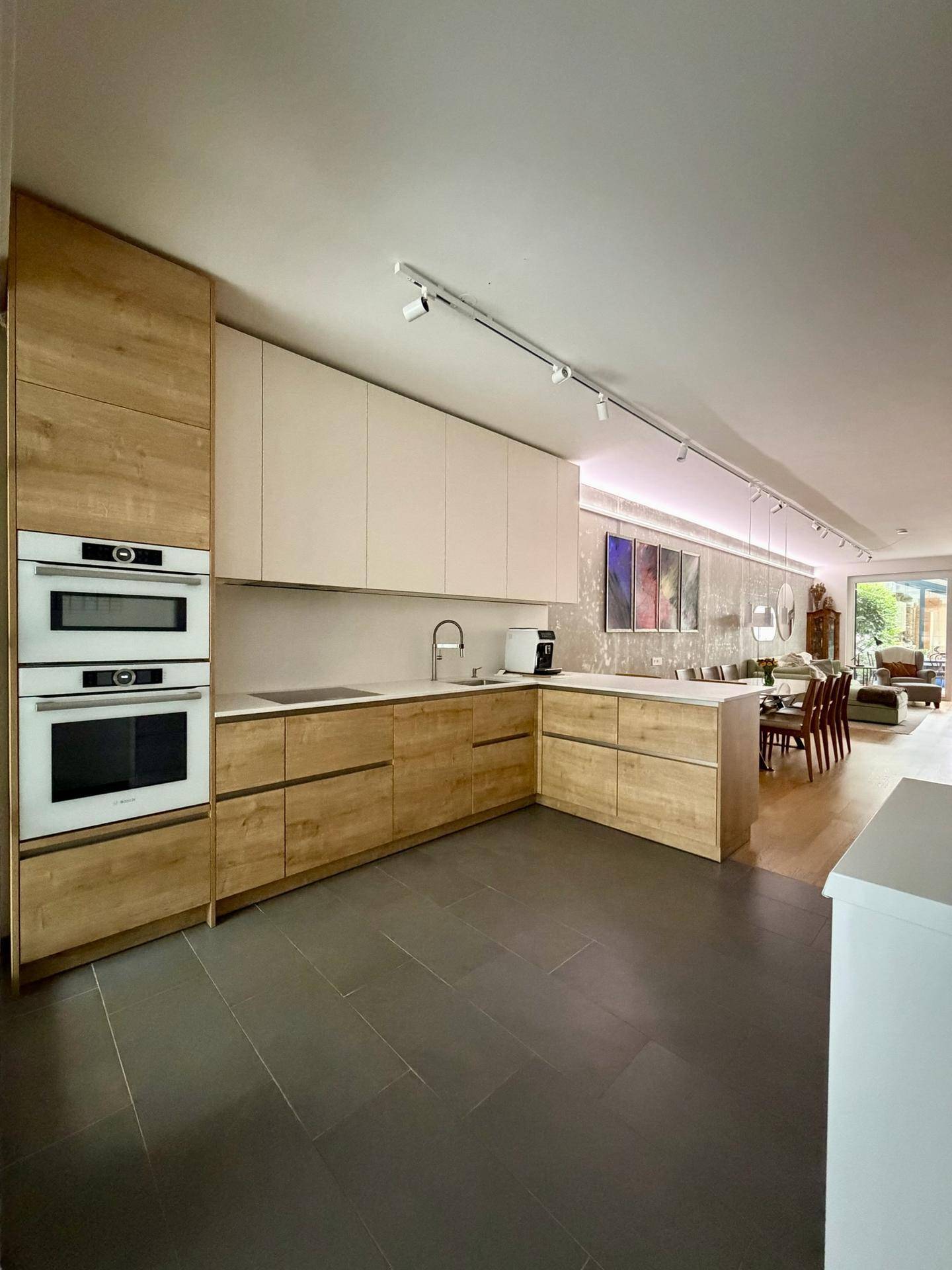 Moderne Holzküche mit integrierten Geräten und offenem Übergang zum Ess- und Wohnbereich.