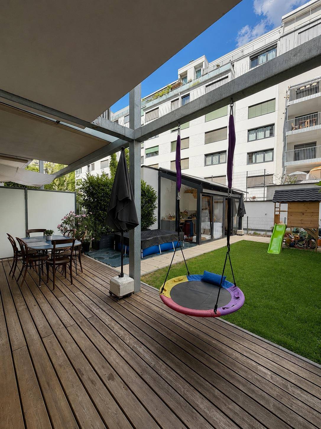 Große Holzterrasse mit Essbereich, Schaukel und Blick auf den grünen Garten.