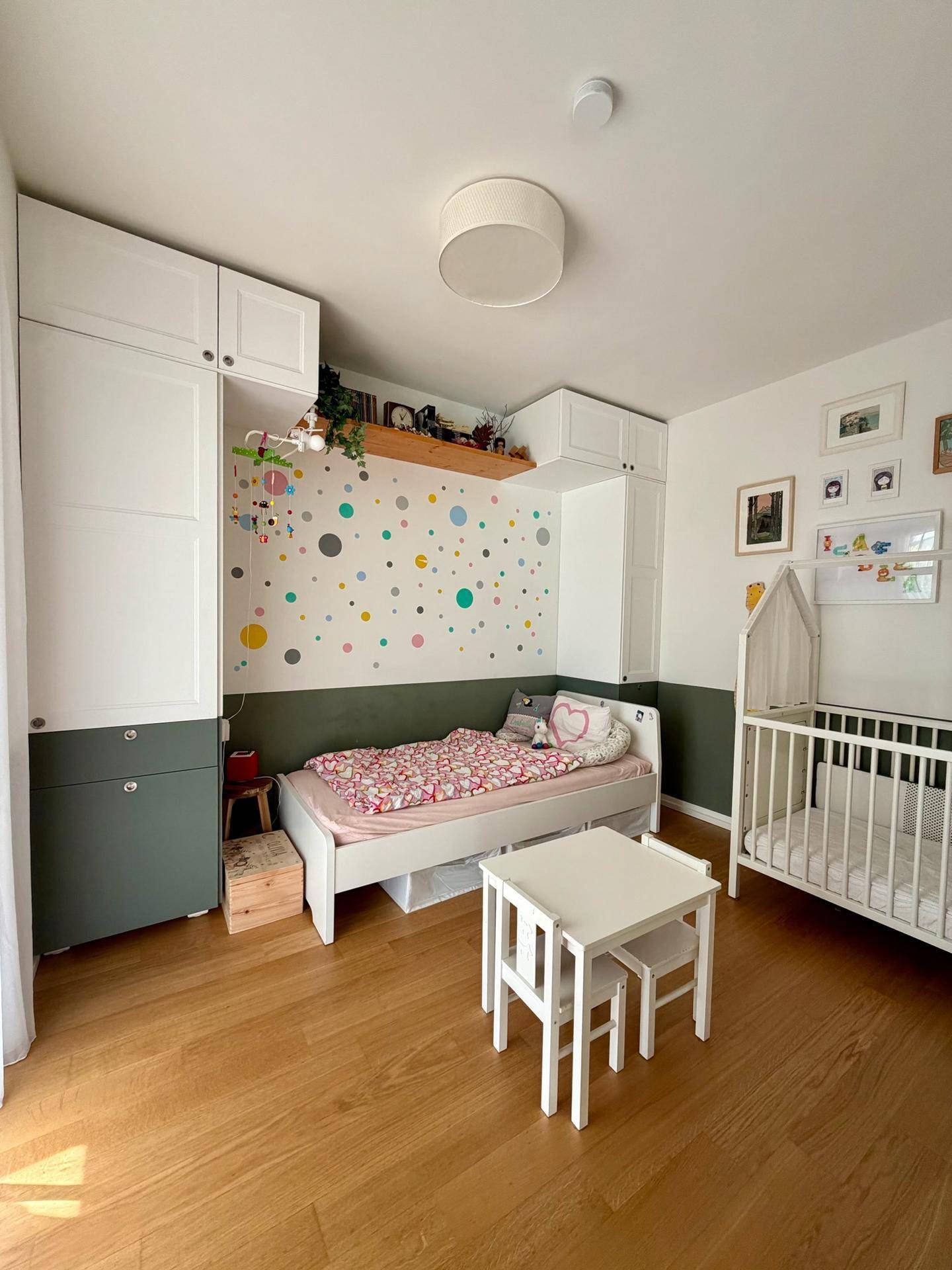Farbenfrohes Kinderzimmer mit Bett, Babybett und spielerischer Wandgestaltung.