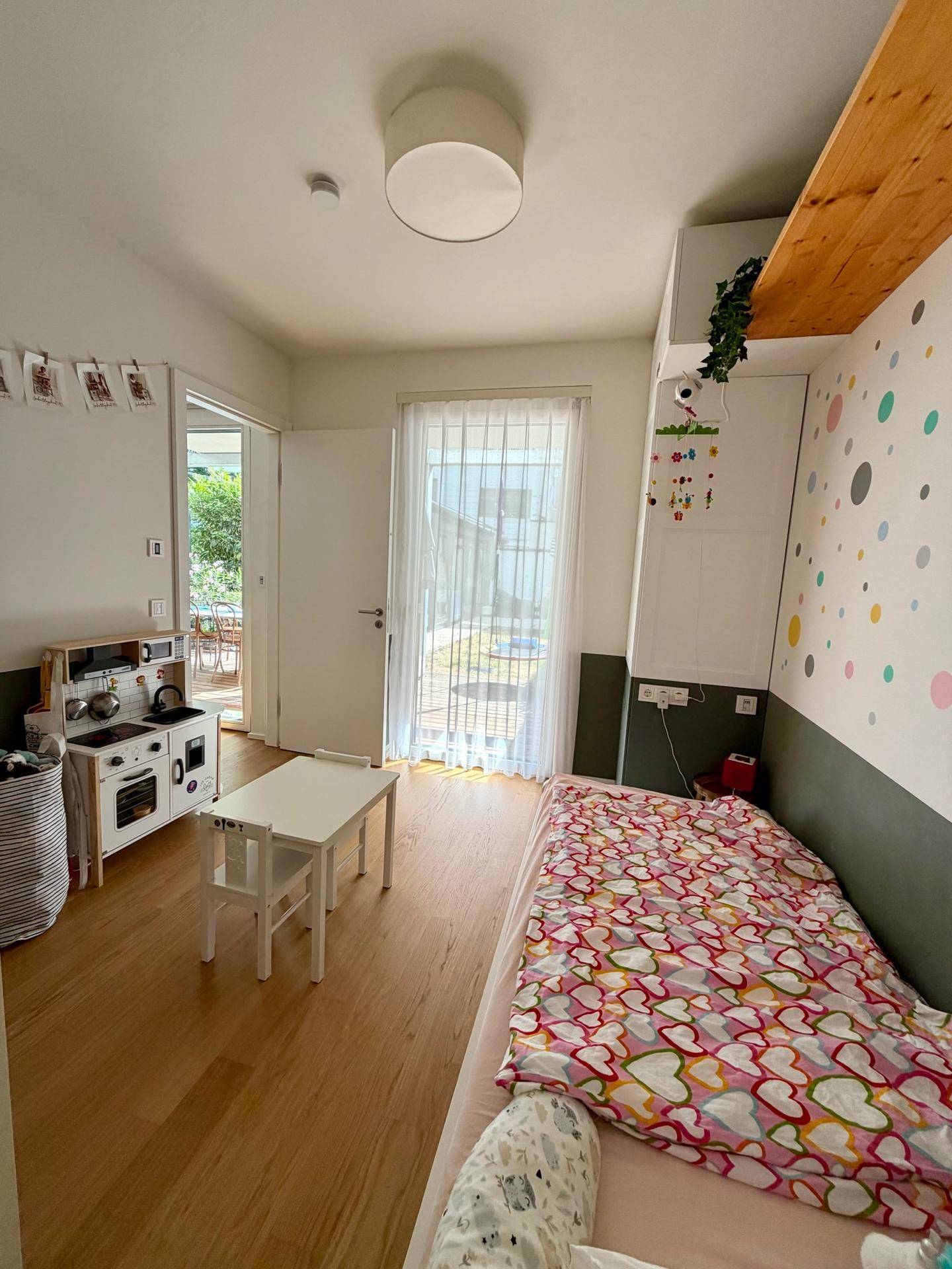 Helles Kinderzimmer mit Bett, kleinem Tisch und Zugang zum Außenbereich.