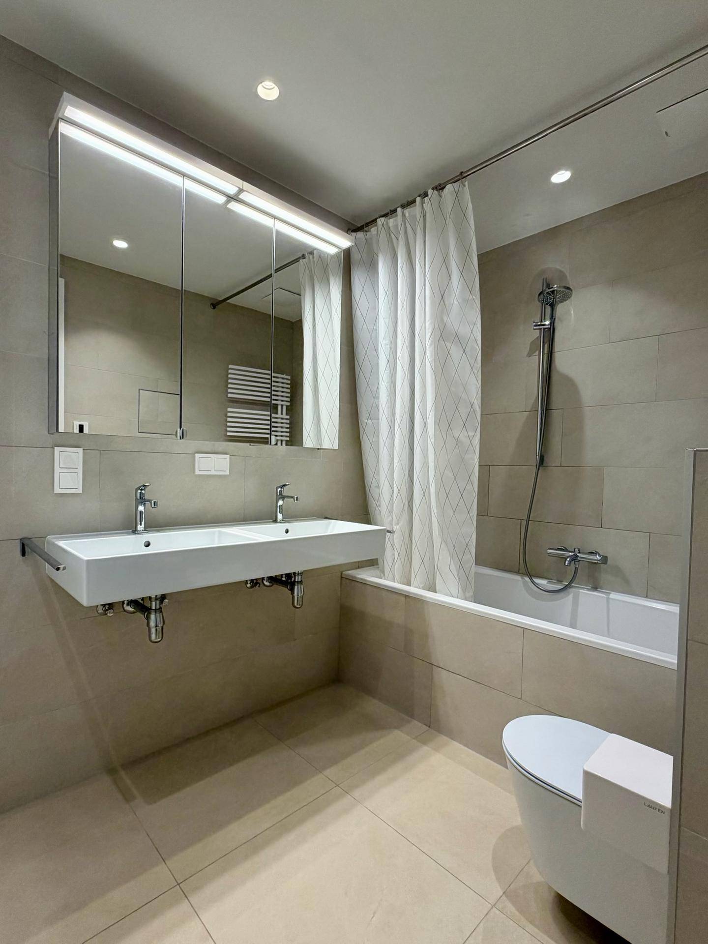 Modernes Badezimmer mit Doppelwaschbecken, Badewanne mit Duschvorhang und Handtuchheizkörper.