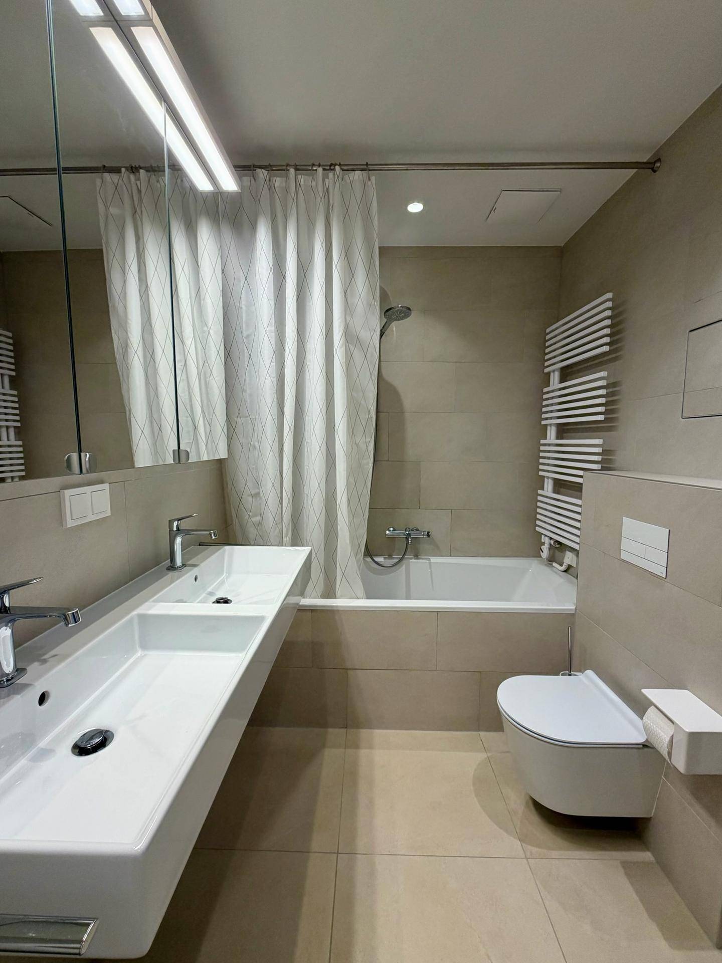 Helles Badezimmer mit Doppelwaschbecken, Badewanne und modernem Handtuchheizkörper.