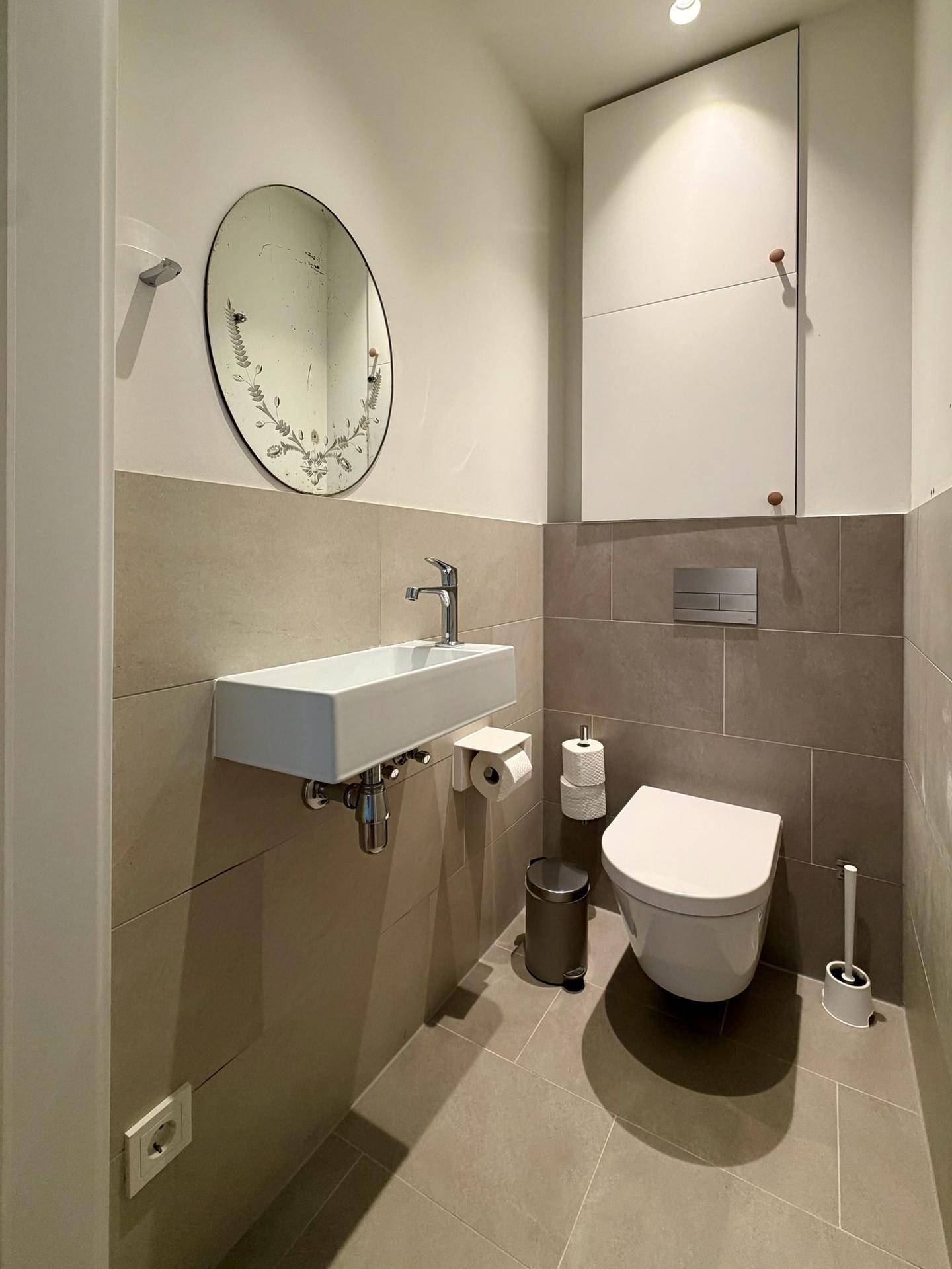 Kleines Gäste-WC mit modernem Waschbecken und ovalem Wandspiegel.
