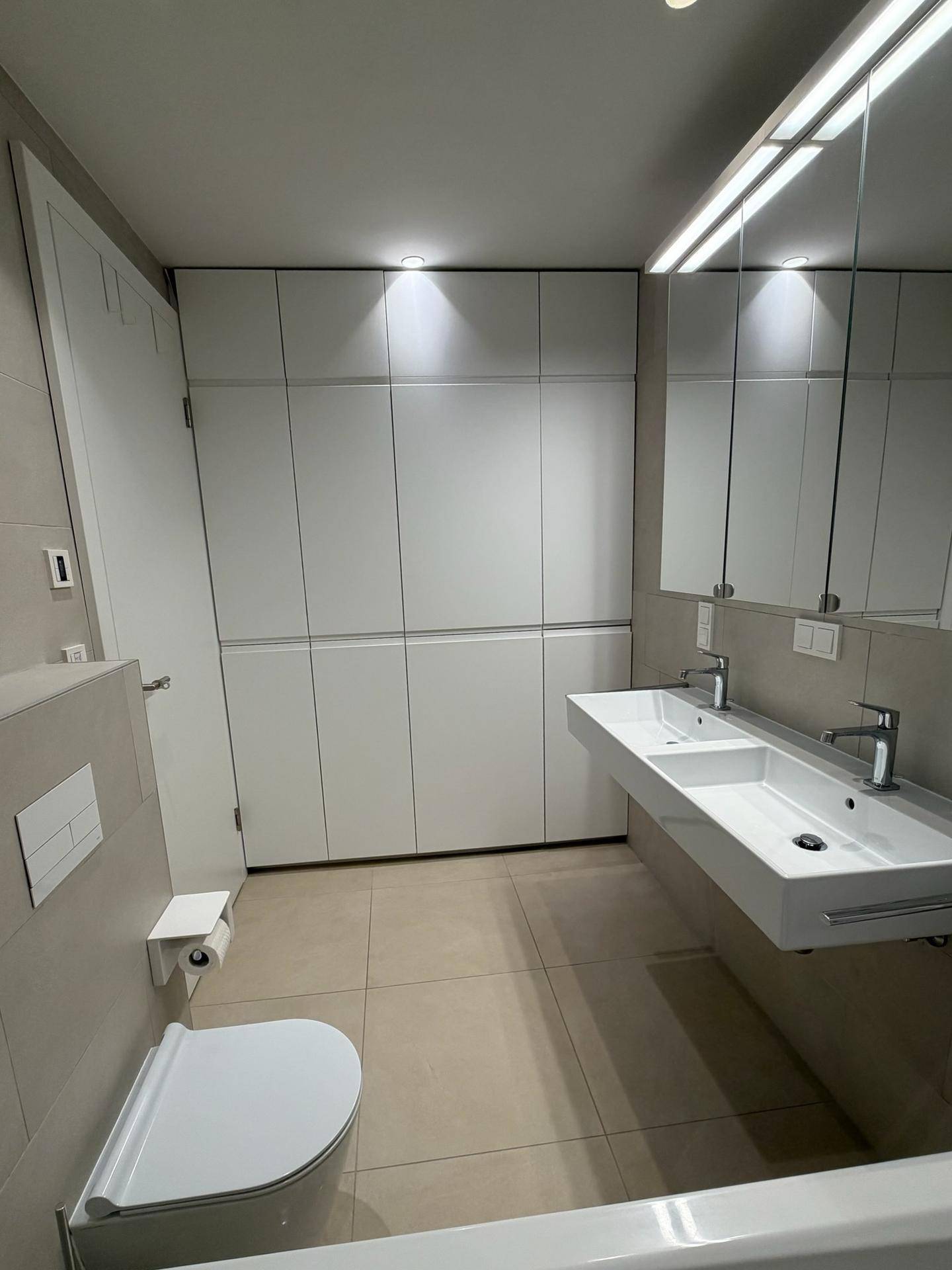 Modernes Badezimmer mit Doppelwaschbecken, Toilette und integrierten Wandschränken.