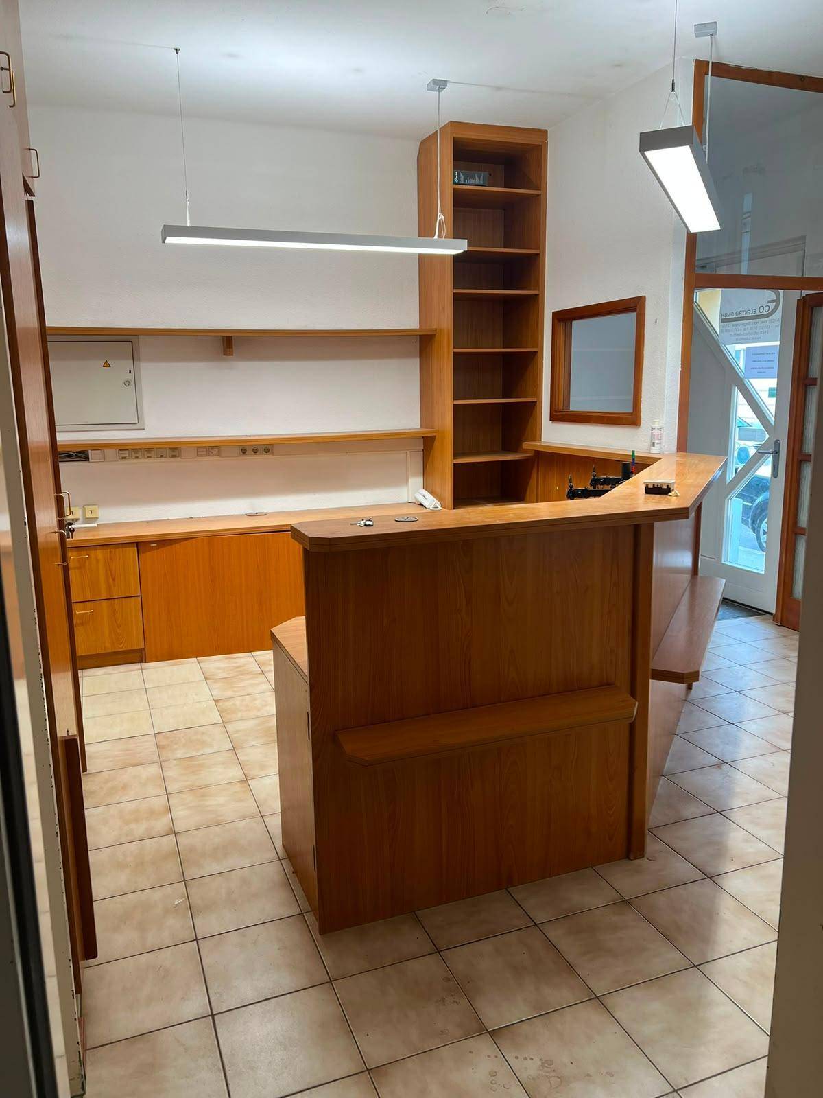 Geräumiger Empfangsbereich oder Büro mit Holztheke, Regalen und modernen Deckenleuchten.