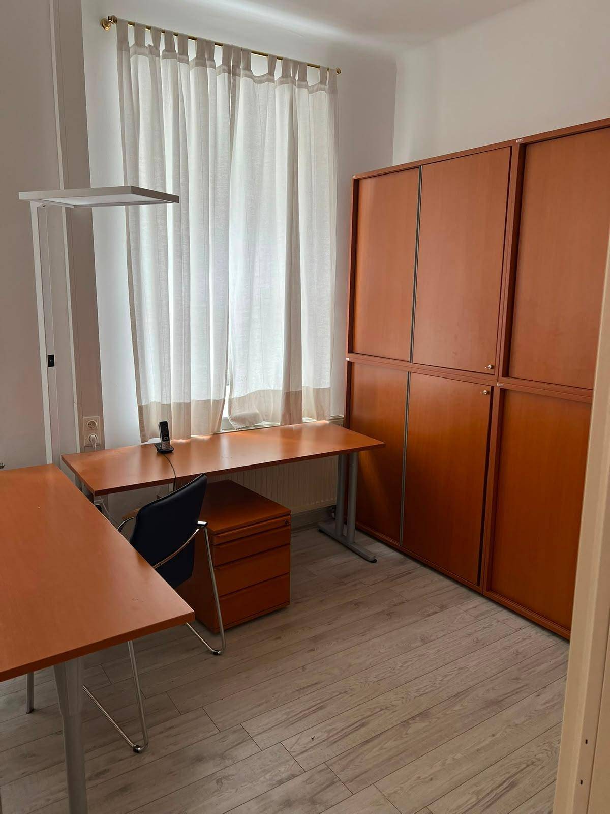 Büro mit zwei Schreibtischen, großen Holzschränken und hellem Laminatboden.