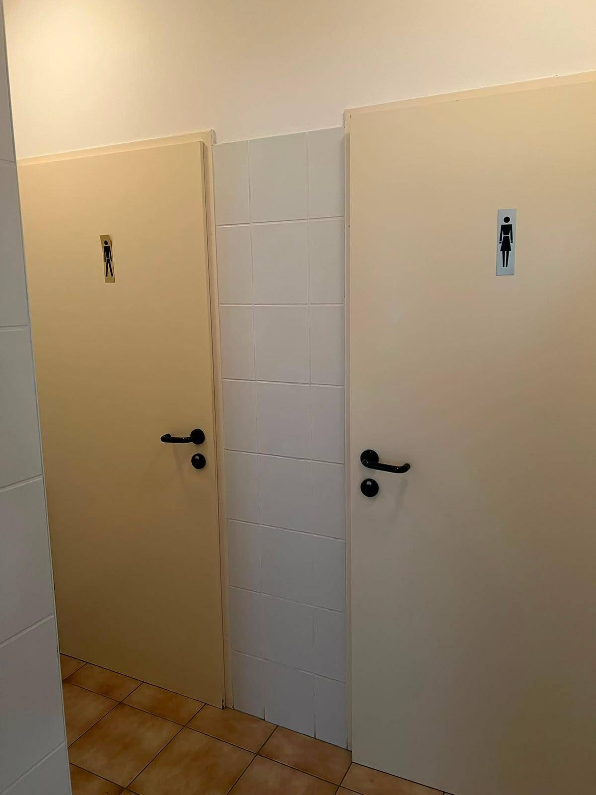 Zwei Toilettenkabinen mit geschlechtsneutralen Symbolen und Fliesenboden.