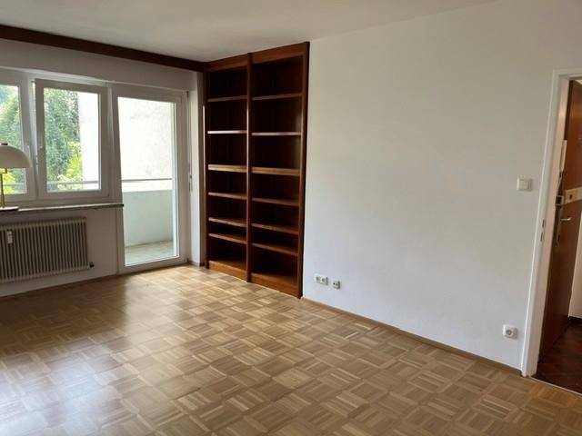 Geräumiges Wohnzimmer mit hellem Parkettboden, weiß gestrichenen Wänden und Zugang zu weiteren Räumen.