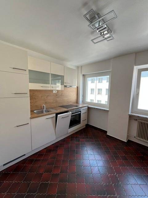 Moderne Küche mit weißen Schränken, Holzarbeitsplatte, Einbaugeräten und zwei Fenstern.