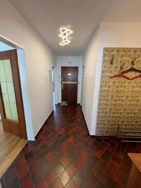 Langer Flur mit gemusterten Bodenfliesen, Garderobe und Blick auf die Eingangstür der Wohnung.
