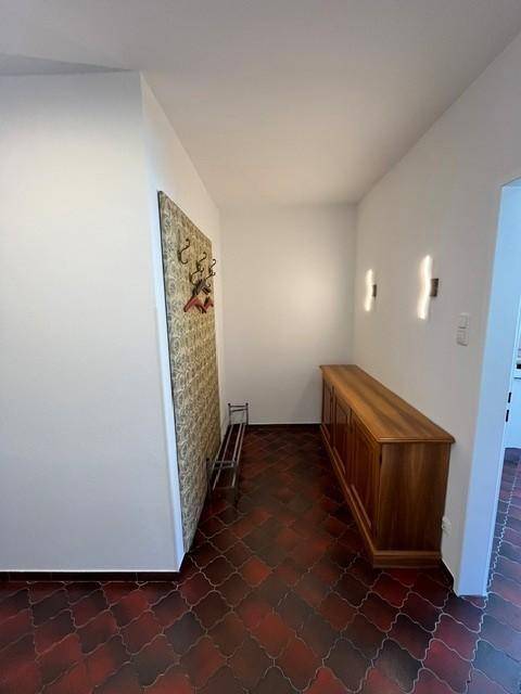Eingangsbereich mit gemusterten Bodenfliesen, einer Holzkommode und einer Garderobe an der Wand.