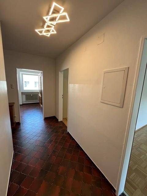 Heller Flur mit auffälligen roten Bodenfliesen und moderner Deckenbeleuchtung, der zu den Zimmern führt.
