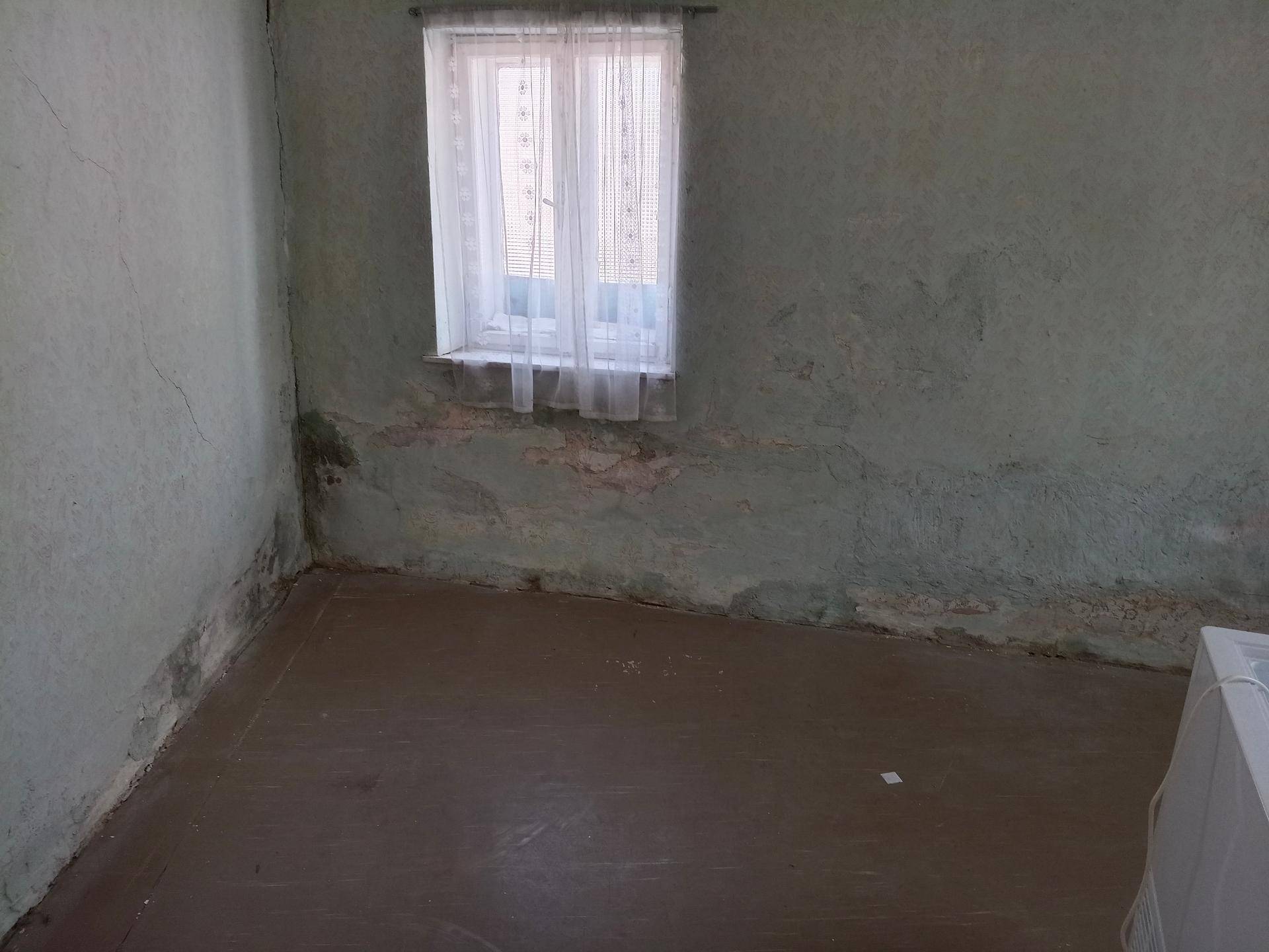 Leeres Zimmer mit grüner Tapete, Holzboden und einem Fenster, renovierungsbedürftig.