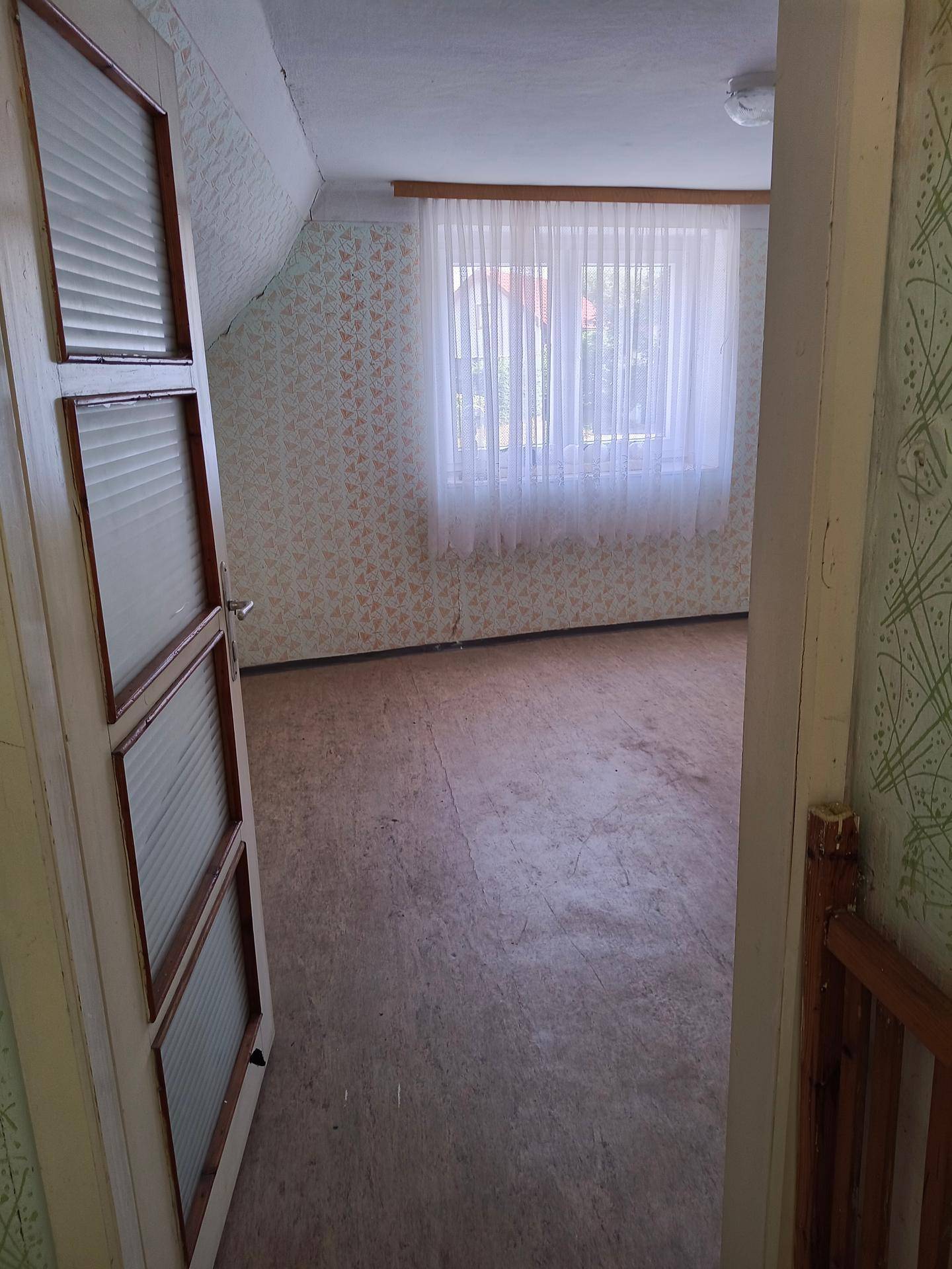 Helles Zimmer mit gemusterter Tapete, Holzboden und Blick aus dem Fenster.