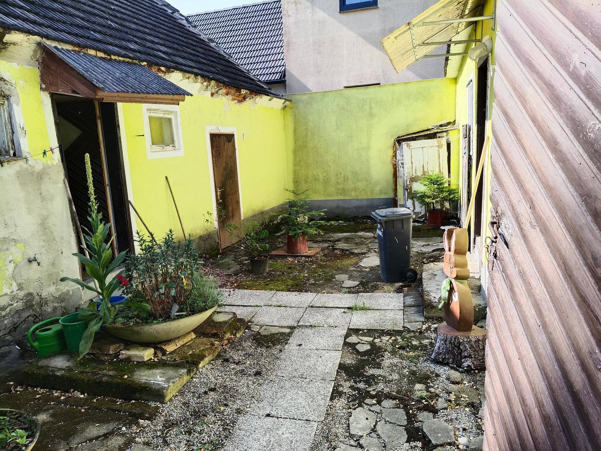 Innenhof mit gelben Wänden, Pflastersteinen und verschiedenen Pflanzen in Töpfen.