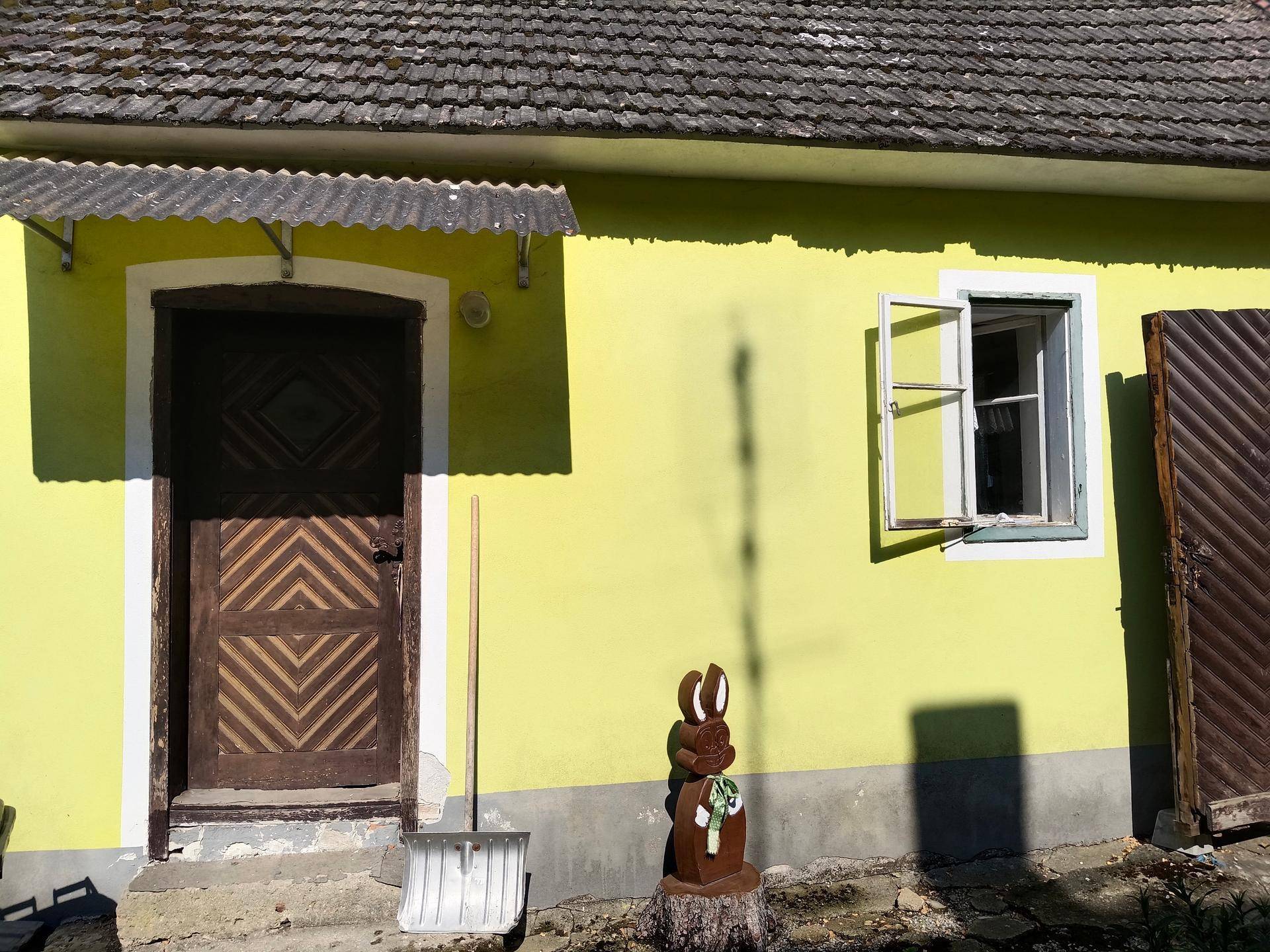 Eingangsbereich eines Hauses mit gelber Fassade, Holztür und geöffnetem Fenster.