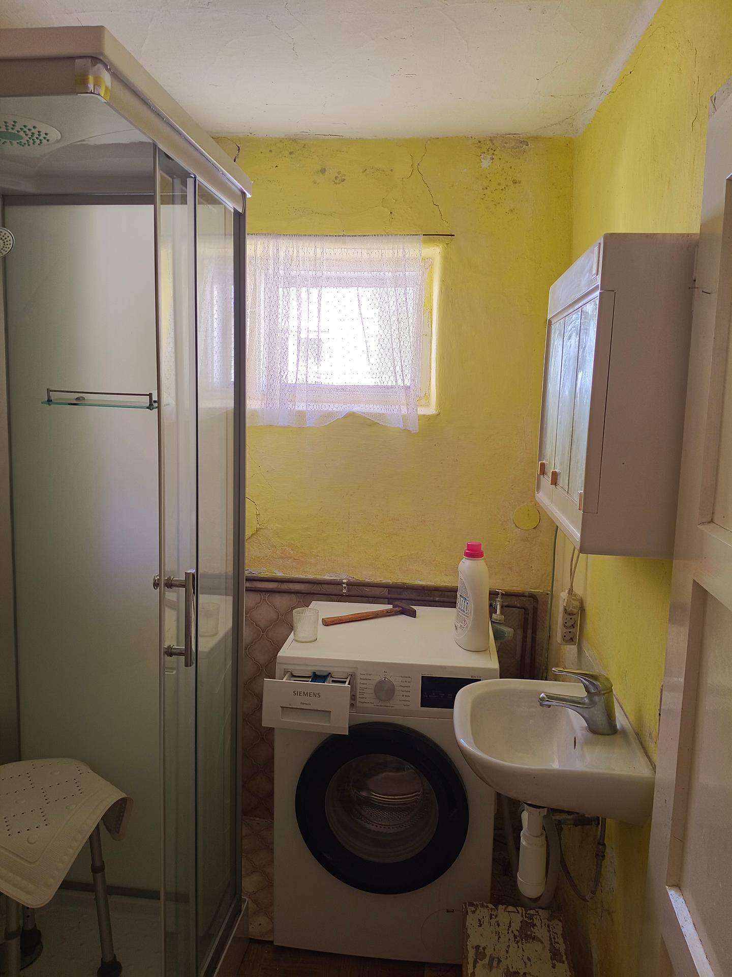 Einfaches Badezimmer mit Dusche, Waschmaschine und kleinem Waschbecken.