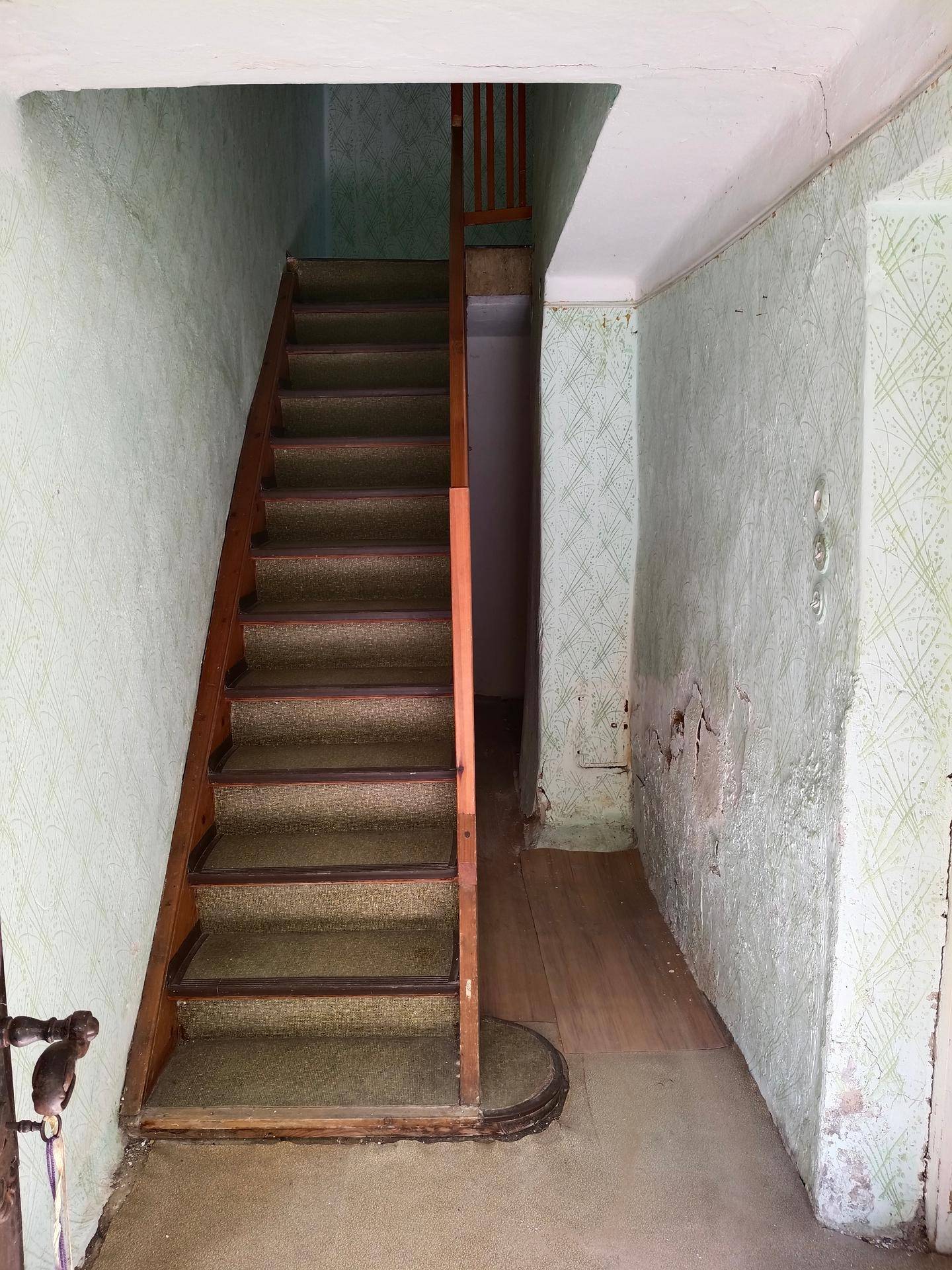 Flur mit Holztreppe und gemusterter Tapete, die in die obere Etage führt.