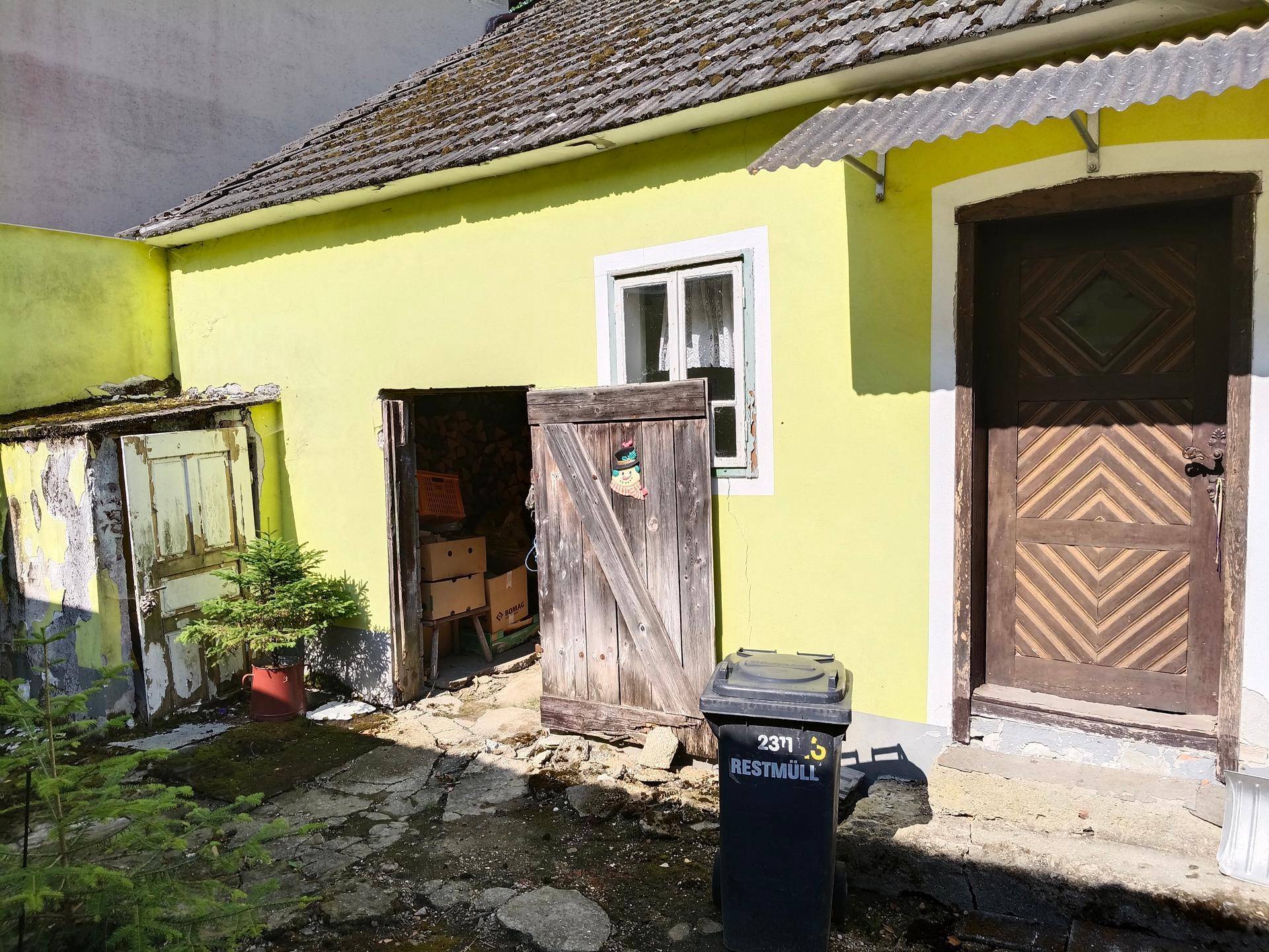 Innenhof mit gelber Fassade, Holztüren und einem Mülleimer.