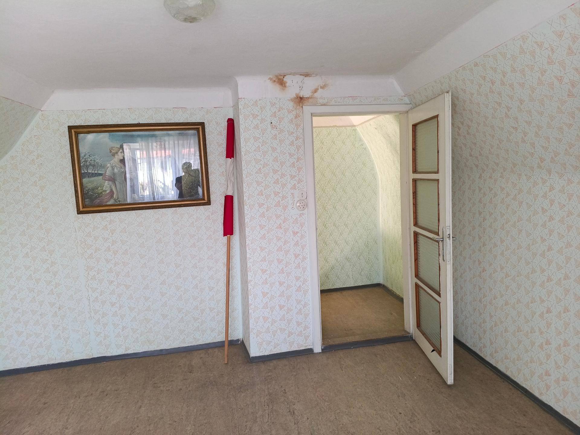 Geräumiges Zimmer mit gemusterter Tapete, Holzboden und offener Tür.
