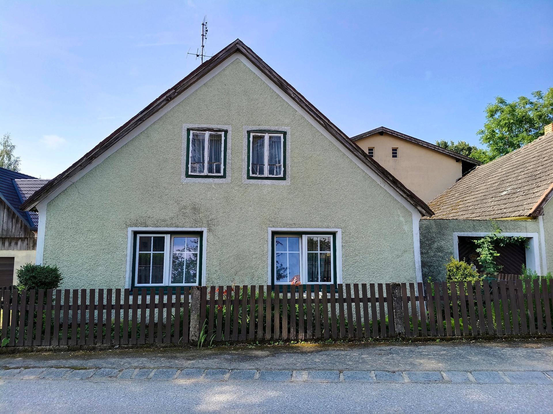 Seitenansicht eines traditionellen Wohnhauses mit hellgrüner Fassade und Satteldach.