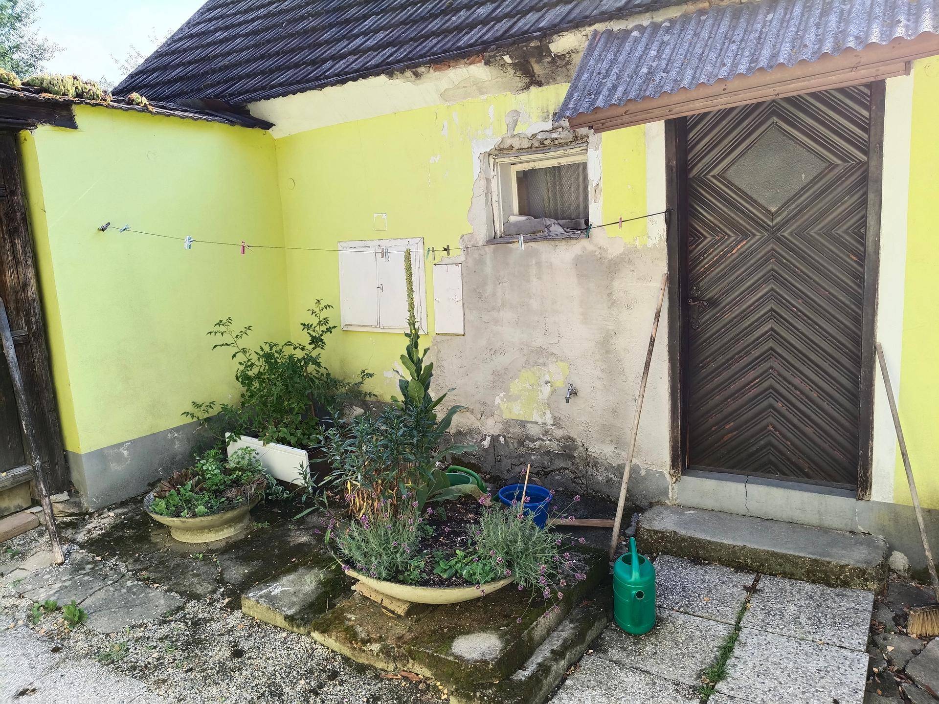 Innenhof mit gelber Fassade, Pflanzgefäßen und einer Gießkanne.