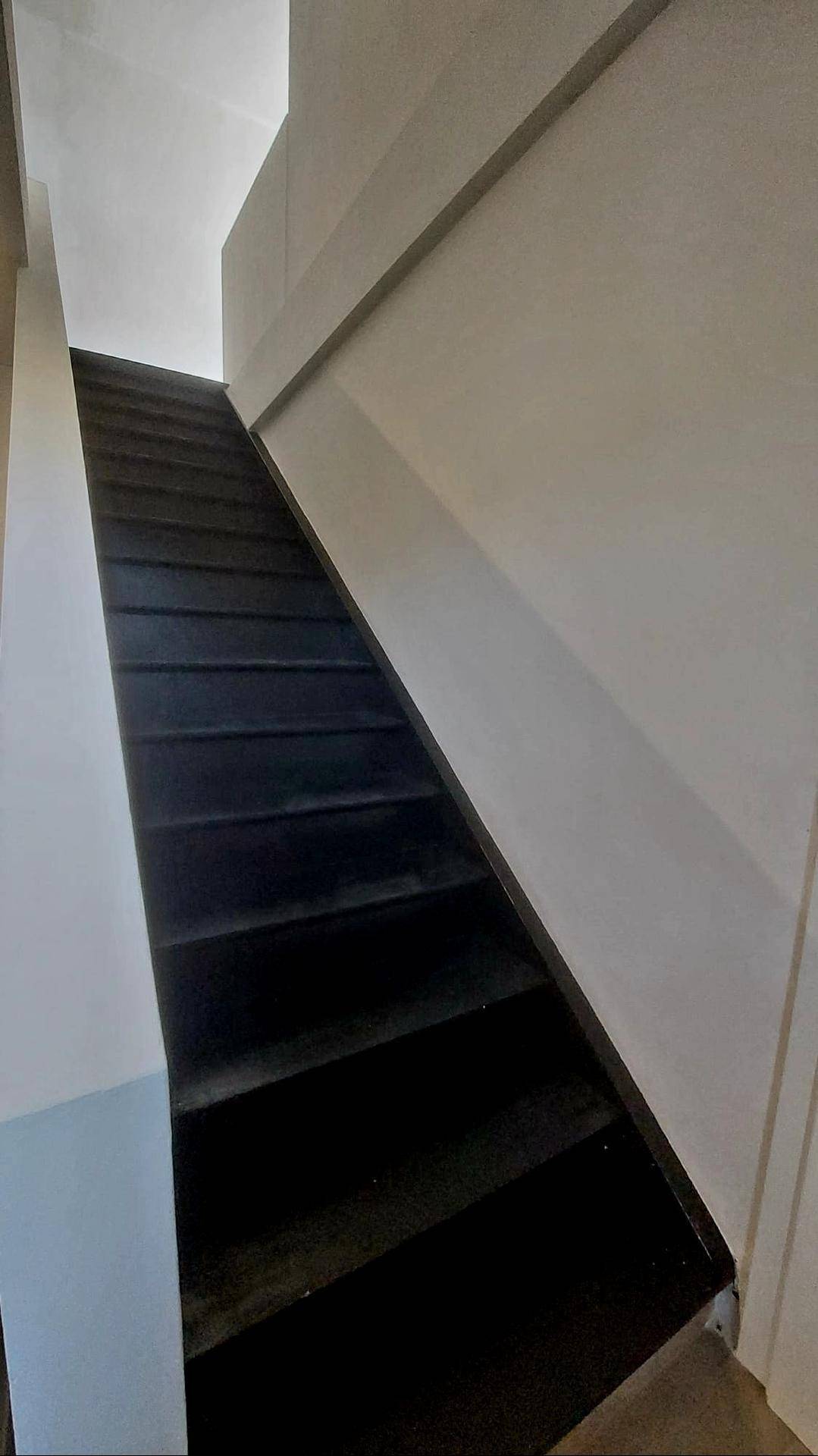 Dunkle Holztreppe mit weißer Wand, die in ein oberes Stockwerk führt.