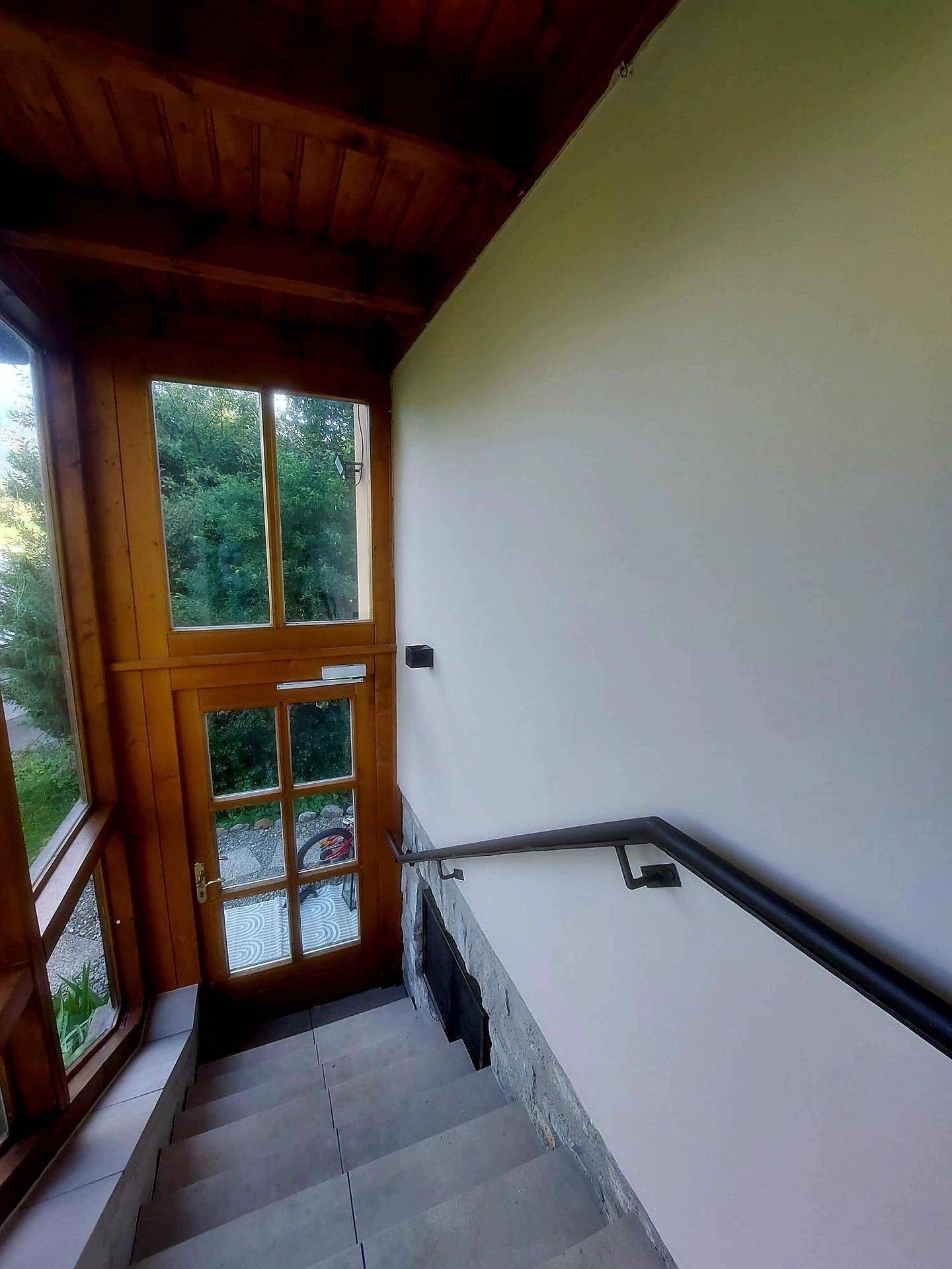 Eingangsbereich mit Steintreppe und Holzverkleidung, führt zu einer verglasten Tür.