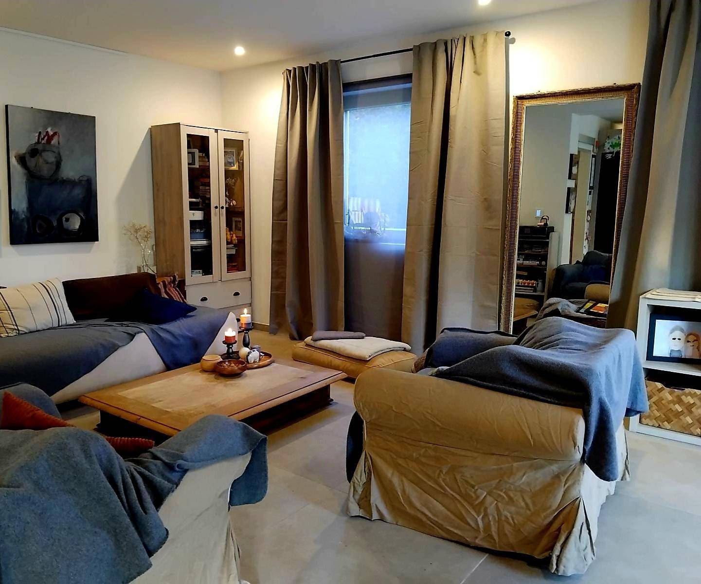 Geräumiges Wohnzimmer mit bequemen Sofas, Holztisch und großem Spiegel, hell beleuchtet.