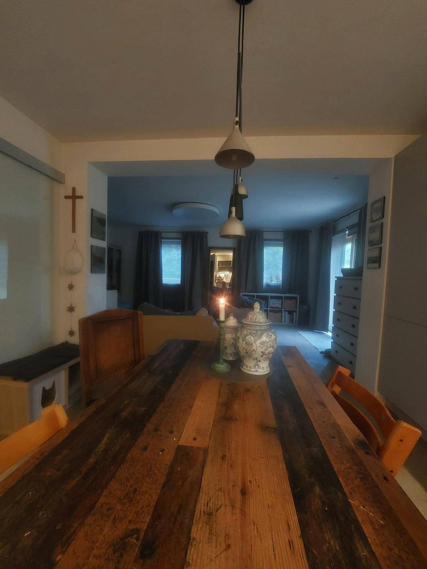 Essbereich mit Holztisch und Blick in ein gemütliches Wohnzimmer, beleuchtet von Kerzen.