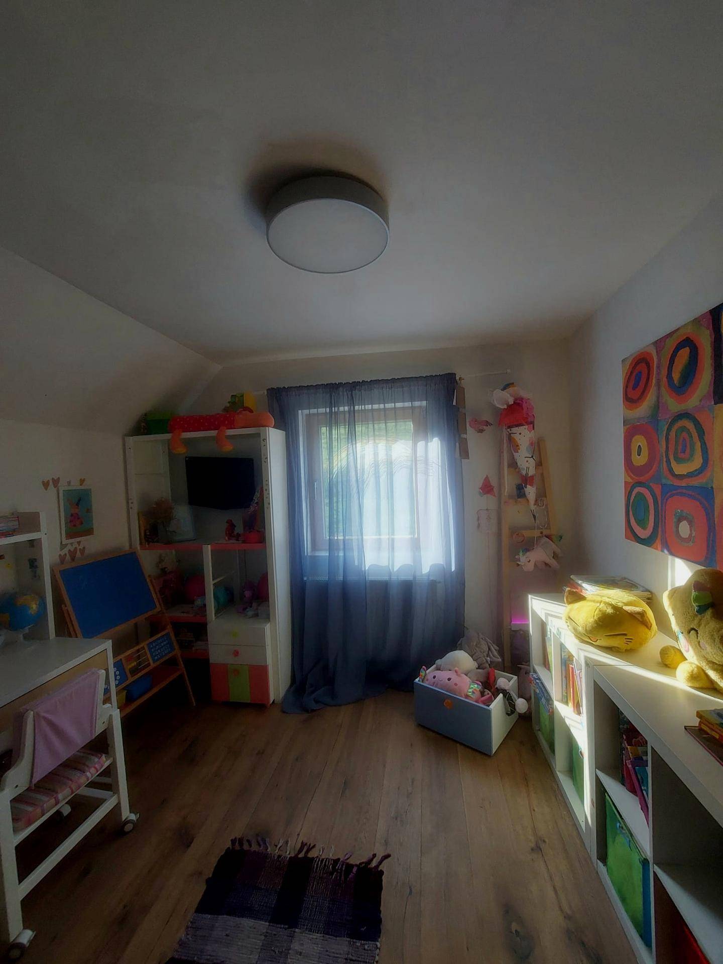 Helles Kinderzimmer mit Spielzeug und Regalen, Holzboden und einem Fenster mit Vorhängen.