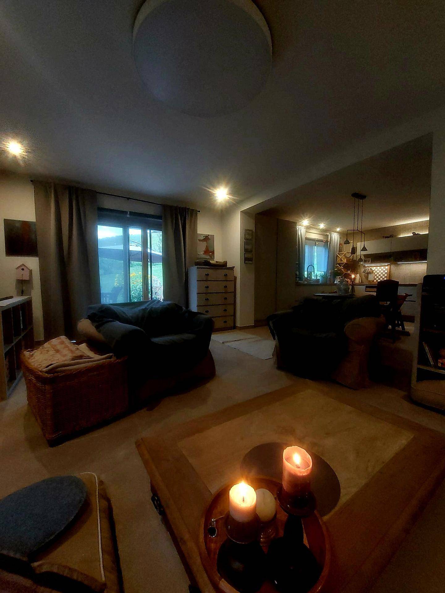 Gemütliches Wohnzimmer mit dunklen Sofas und Kerzenlicht, verbunden mit der Küche.