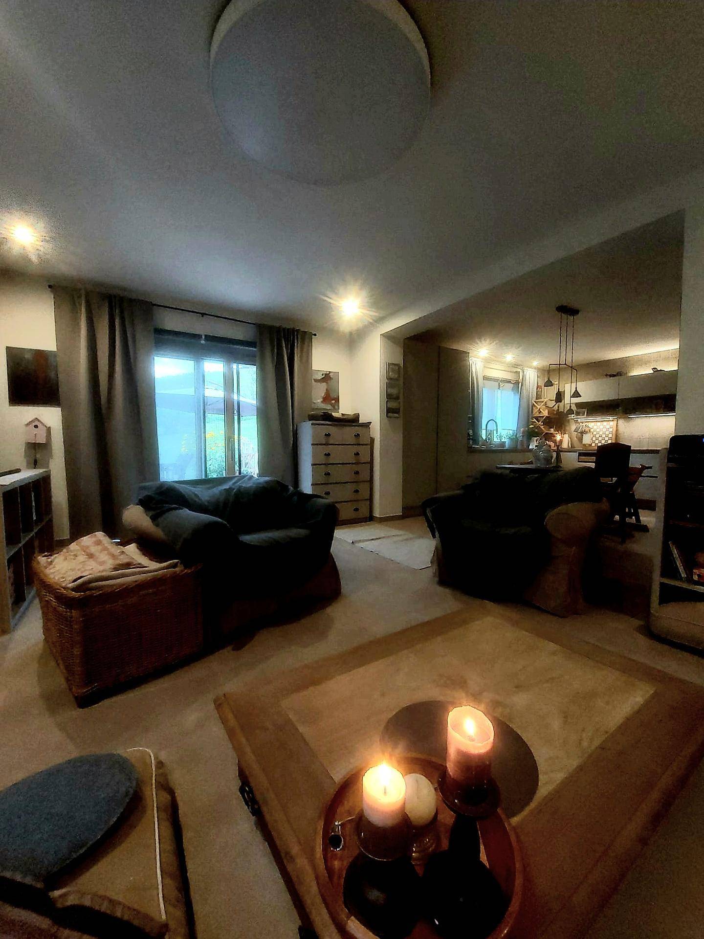 Gemütliches Wohnzimmer mit Kerzenlicht und Blick auf den angrenzenden Küchenbereich.