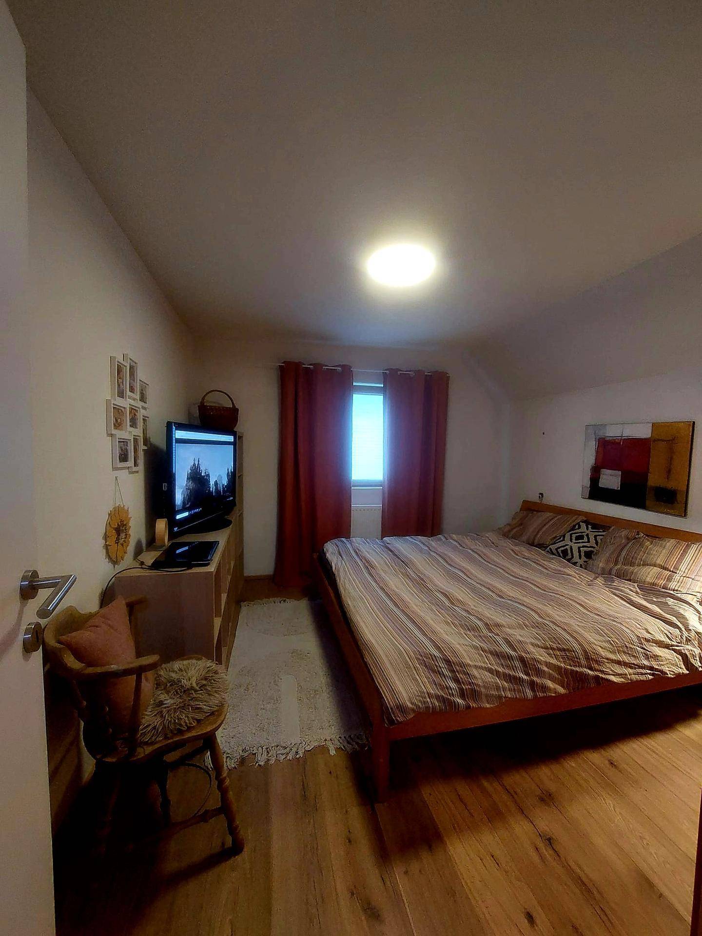 Gemütliches Schlafzimmer mit Holzbett, Holzboden und einem kleinen Fenster, unter Dachschräge.