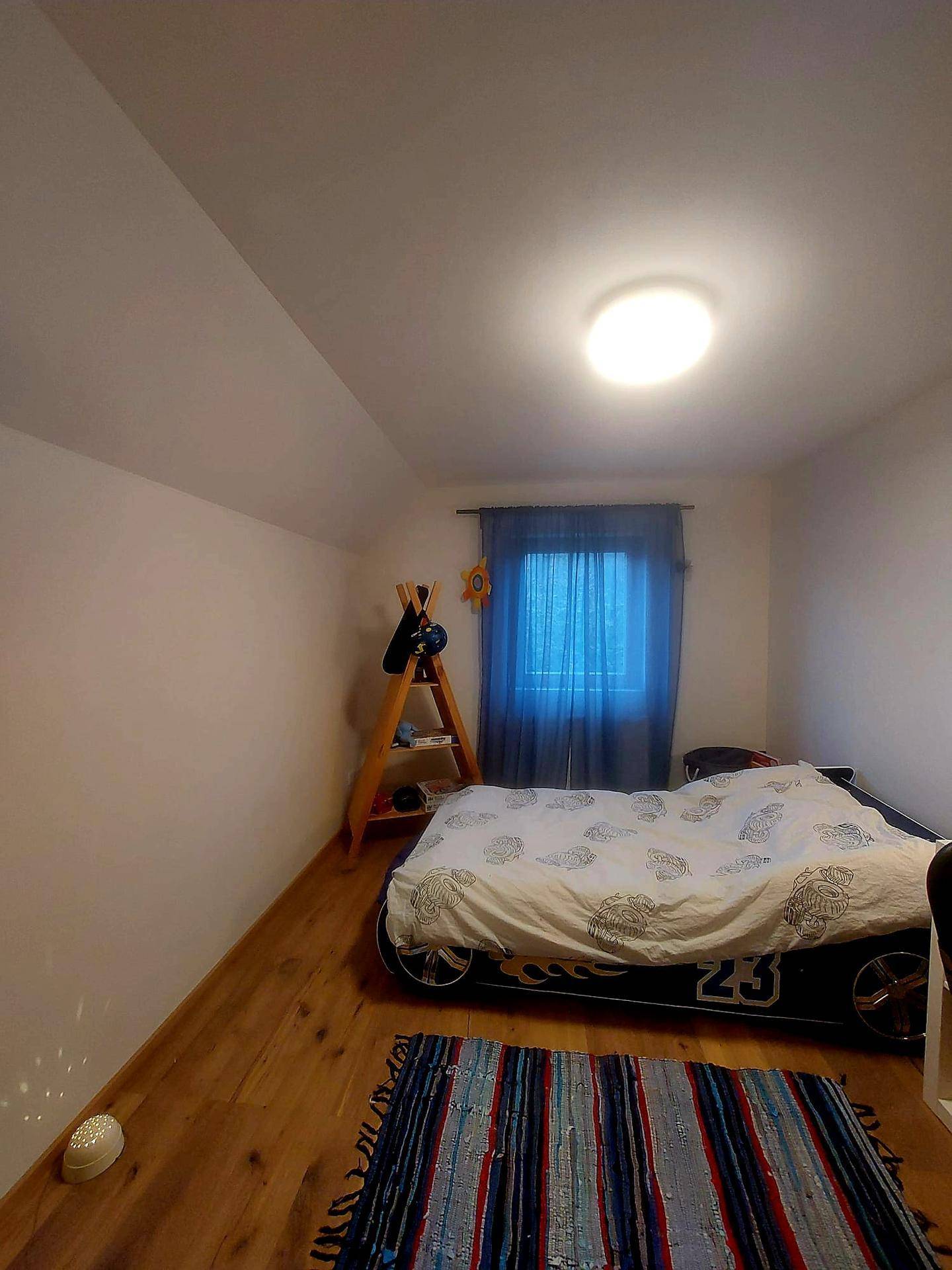 Kinderzimmer mit Rennwagenbett, Holzfußboden und einem Fenster mit blauen Vorhängen.