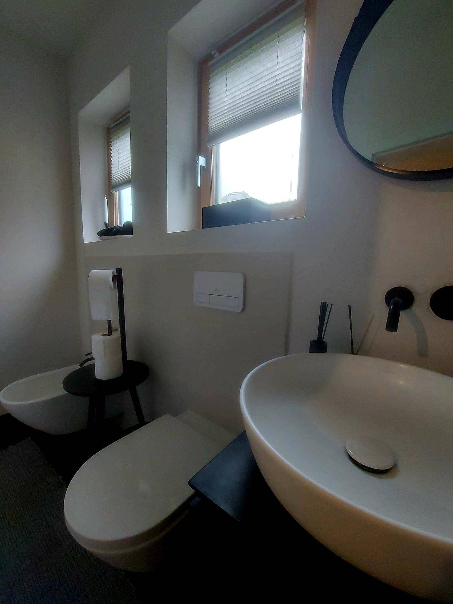 Helles WC mit modernem Waschbecken, Toilette und Bidet, beleuchtet durch ein Fenster.