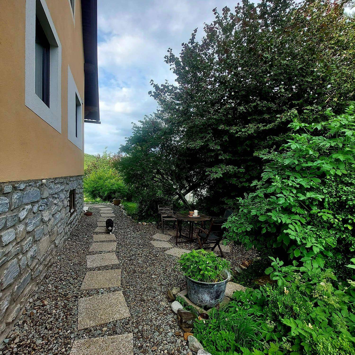 Seitlicher Gartenbereich des Hauses mit Steinweg, Kies und einer kleinen Sitzecke im Grünen.
