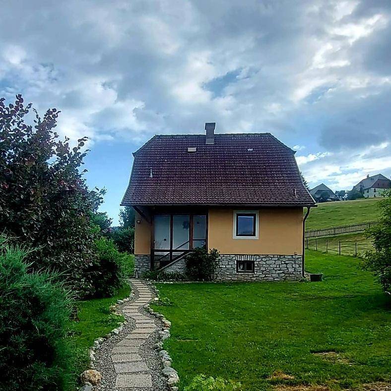 Charmantes Landhaus mit rotem Ziegeldach und grünem Vorgarten unter dramatischem Himmel.