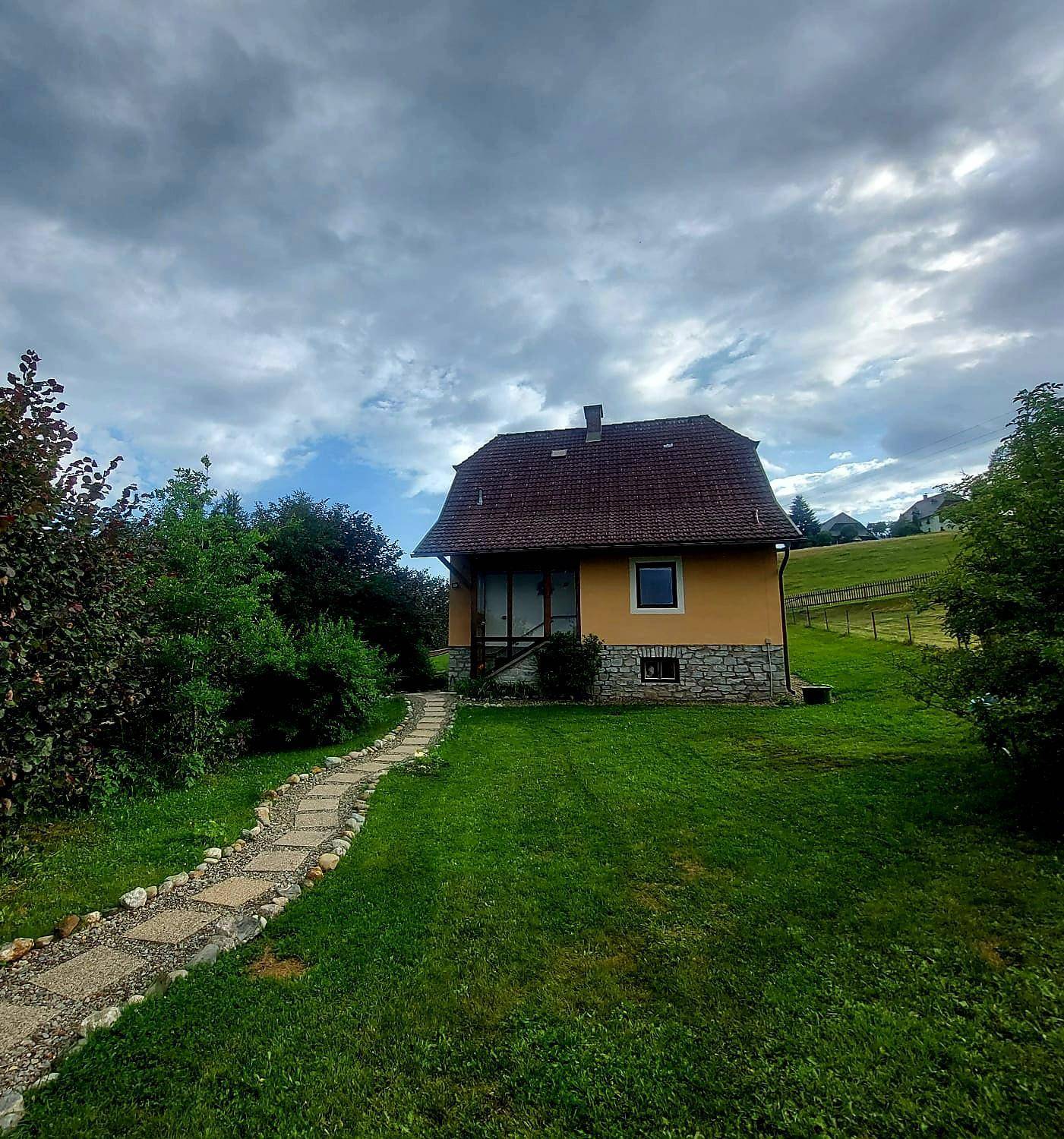 Ländliches Einfamilienhaus mit gepflegtem Garten und Steinweg unter bewölktem Himmel.