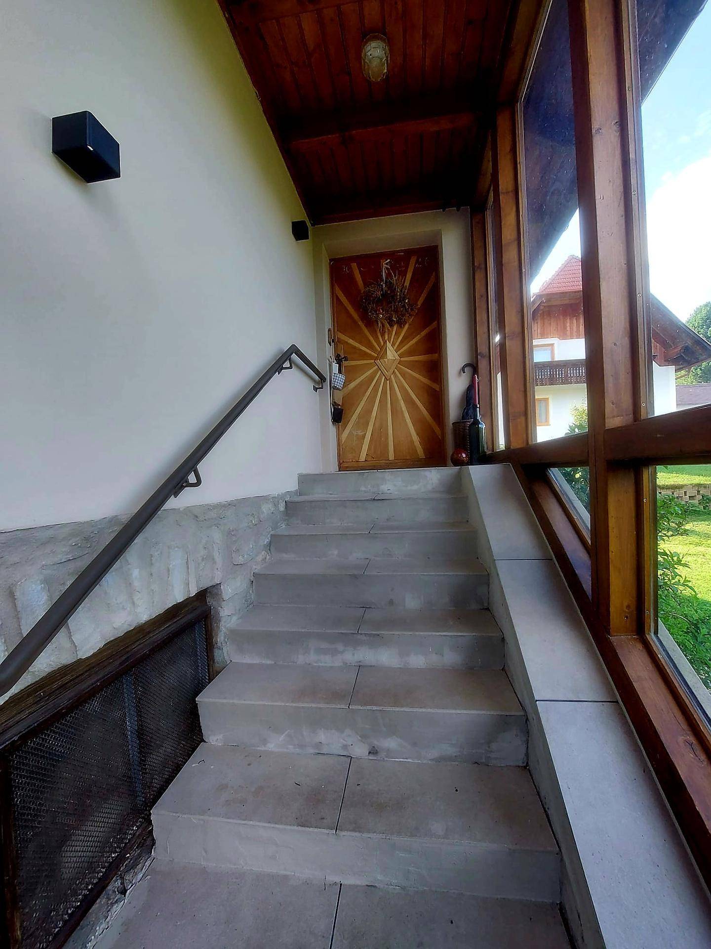 Eingangsbereich des Hauses mit Steintreppe und Holzverkleidung, umgeben von viel Grün.