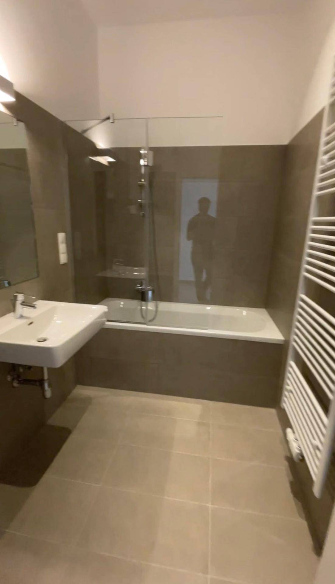 Modernes Badezimmer mit Badewanne, Duschabtrennung und beheiztem Handtuchhalter.